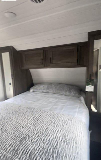 Cozy RV rental bedroom featuring a large bed with white bedding, overhead storage cabinets, and a side closet.. Forest River Evo 2022