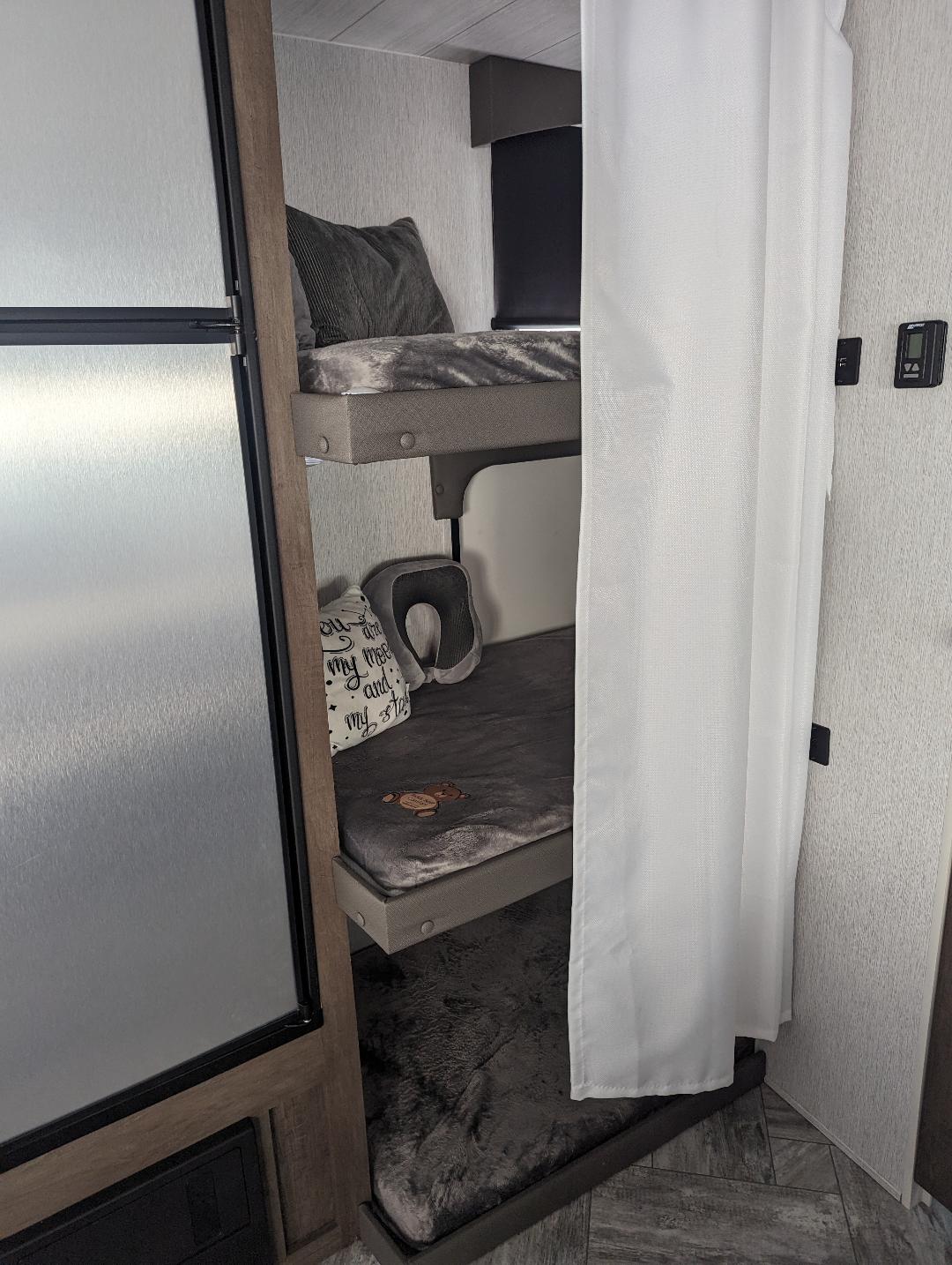 Triple bunk beds with plush grey bedding in an RV rental, offering cozy sleeping space for road trips.. Forest River Evo 2022
