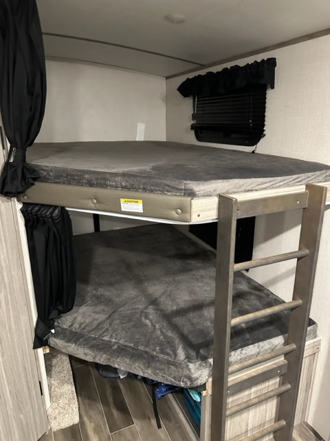 Inside an RV rental, featuring comfortable bunk beds with gray mattresses and a privacy curtain, maximizing sleeping space.. Keystone RV Passport GT 2022
