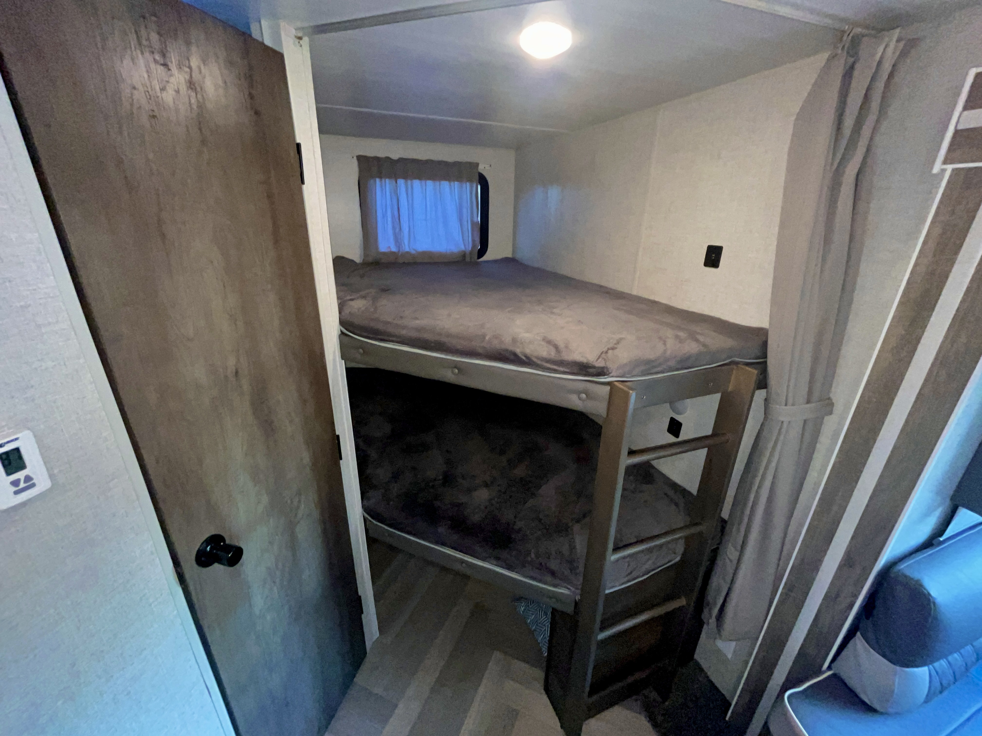 RV rental's compact sleeping area: stacked bunk beds with grey bedding, window, and door.. Forest River Wildwood 2021