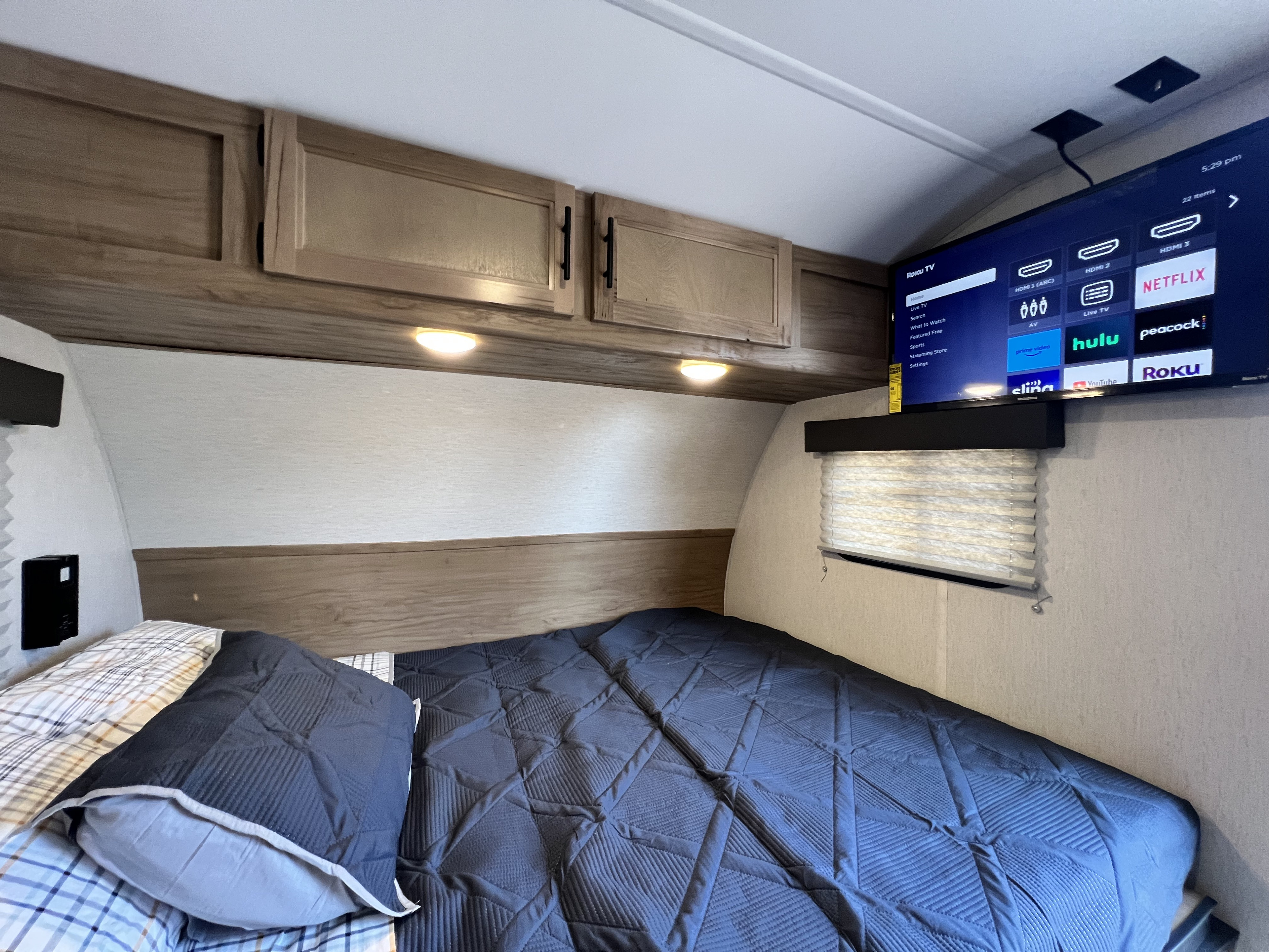 Inside an RV rental: a compact bedroom with a bed, overhead cabinets, and a Roku TV for your road trip comfort.. Forest River Cherokee Wolf Pup 2023