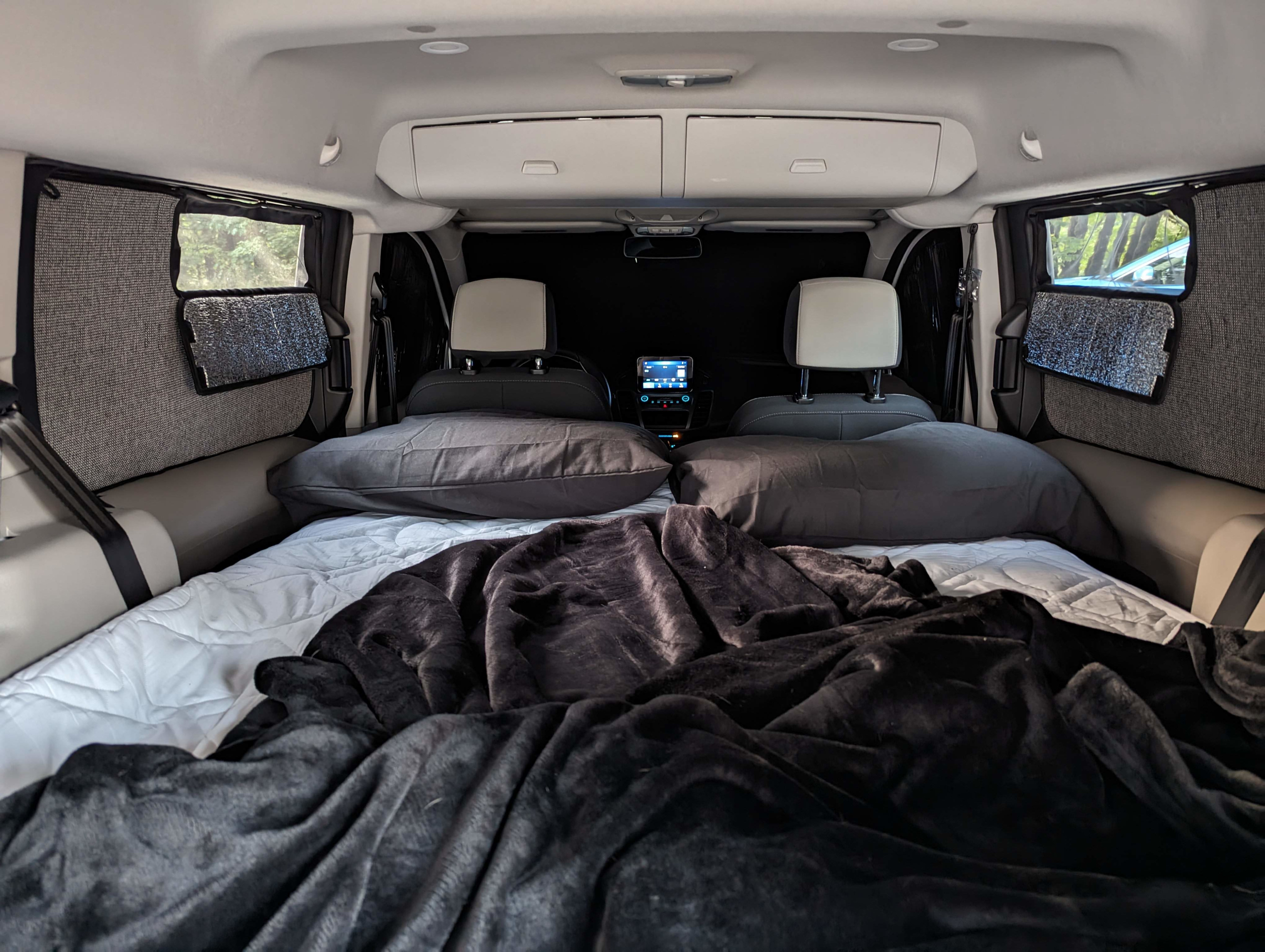 Cozy camper van interior showing a bed setup with pillows, blankets, and window covers. Perfect for an RV rental adventure.. Ford Transit 2022