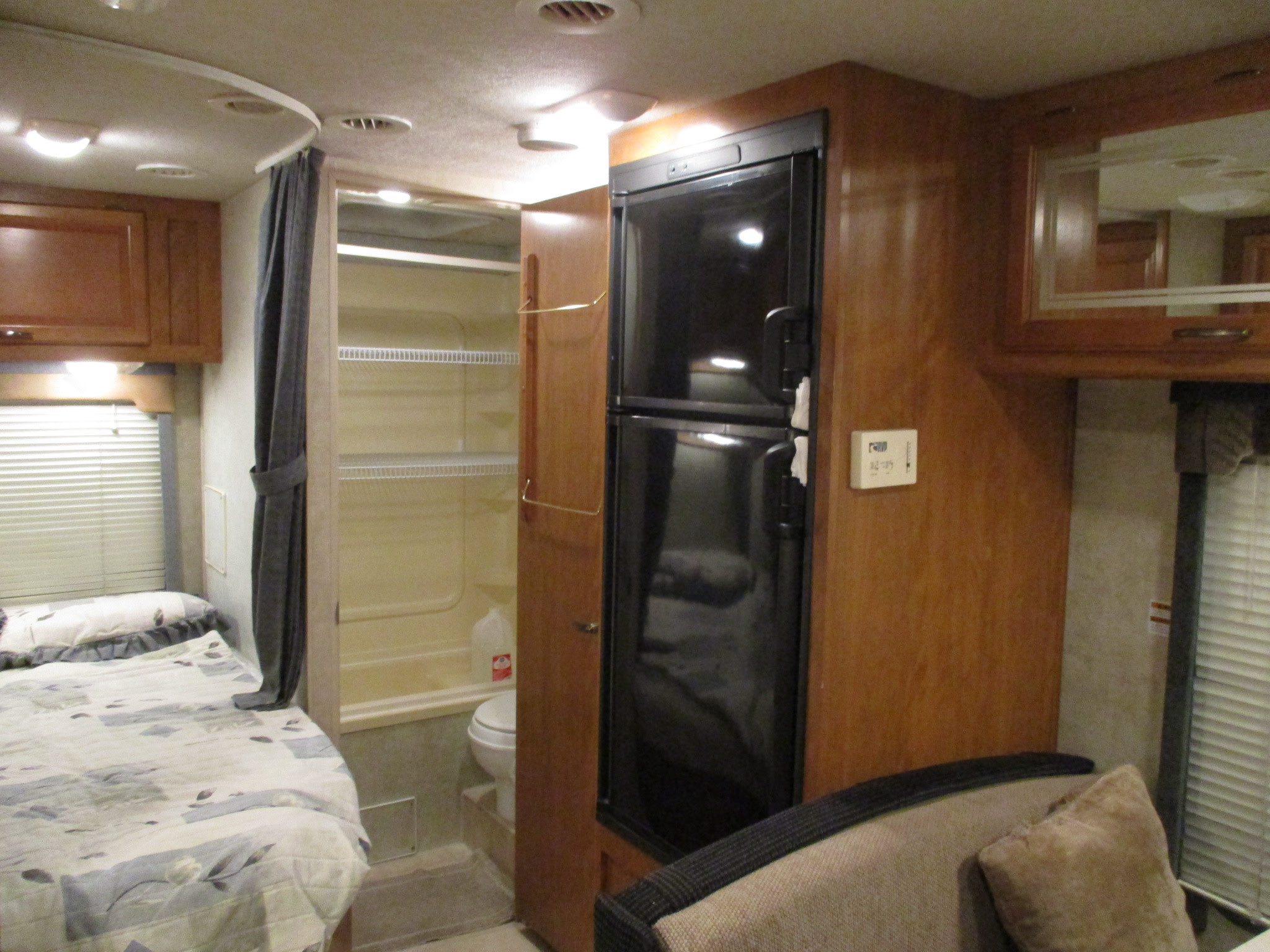 Spacious RV rental interior features: a made bed, open bathroom with toilet, full-size refrigerator, and wood cabinetry.. Tioga Tioga Motorhome 2005