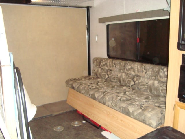 RV rental interior: versatile living space with a patterned sofa, window, and a light-colored wall panel.. Carson Trailer Rebel 14 Toyhauler 2006
