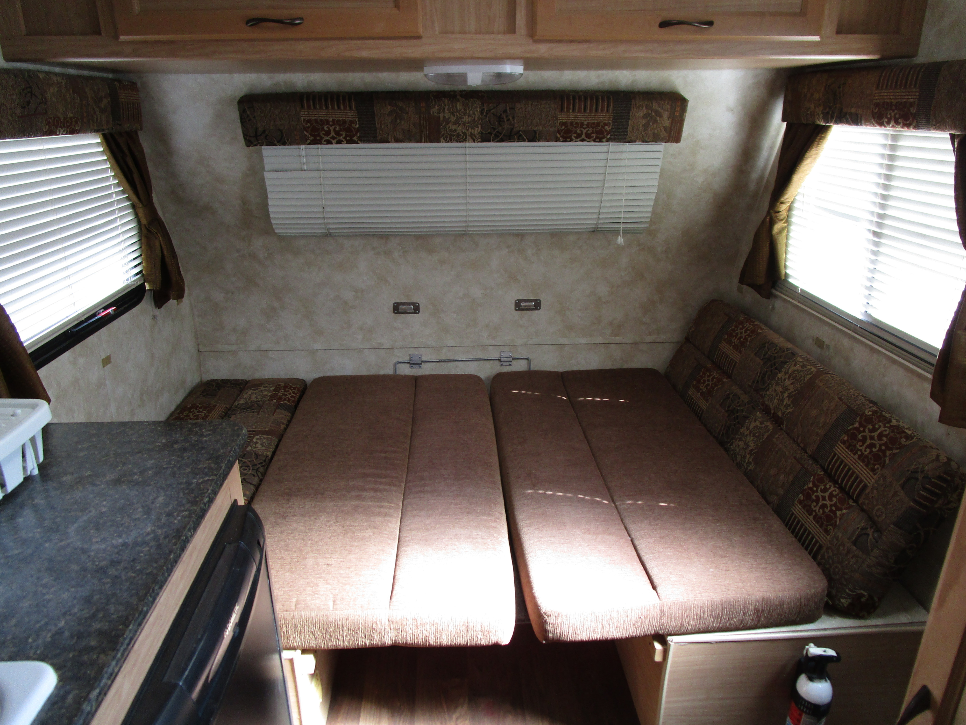 Inside an RV rental, featuring a convertible bed/dinette area, windows with blinds, and a practical kitchen counter.. Econ 14 2014