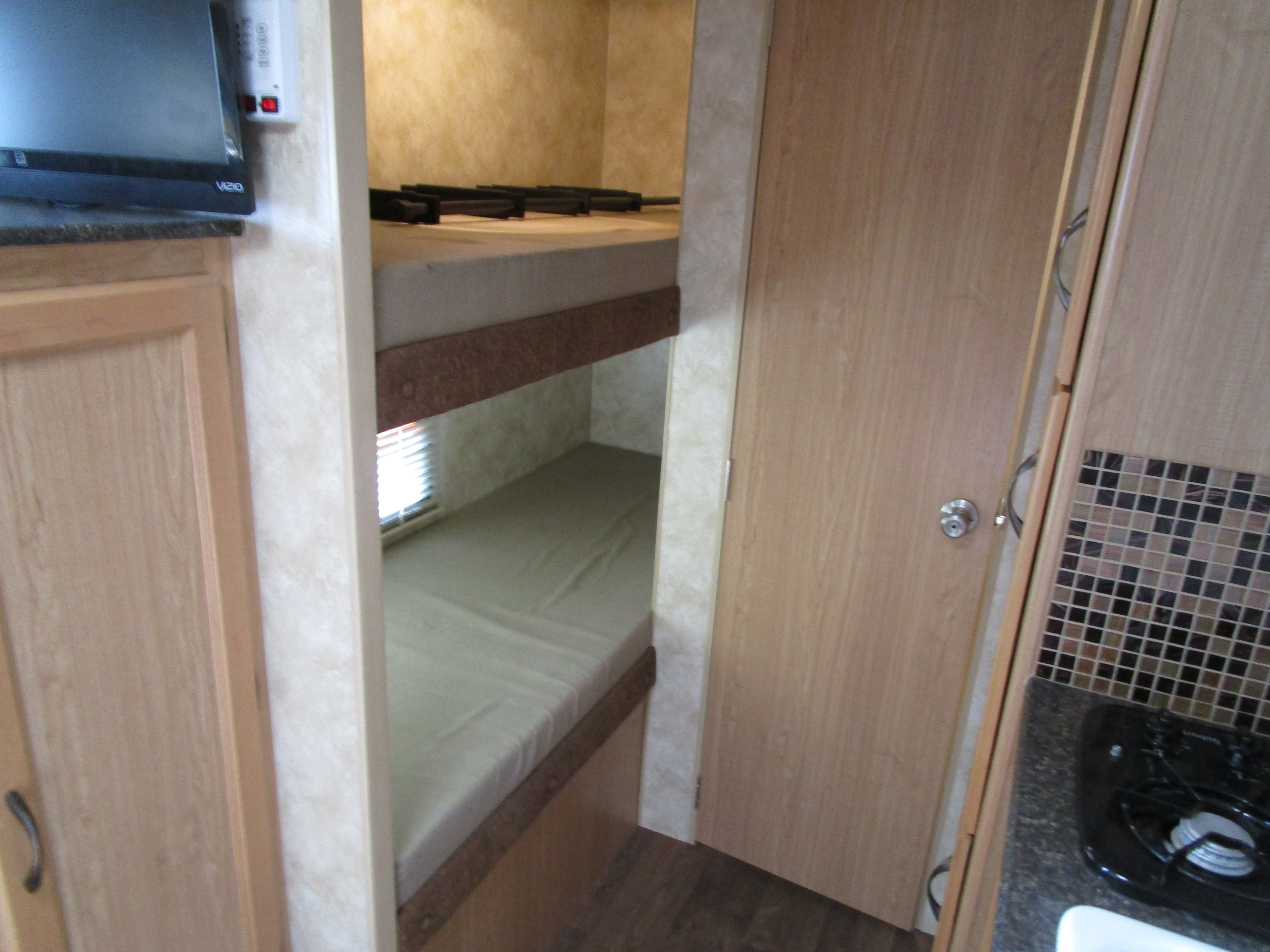 Interior view of an RV rental featuring cozy bunk beds, a TV area, and a compact kitchen space.. Econ 14 2014
