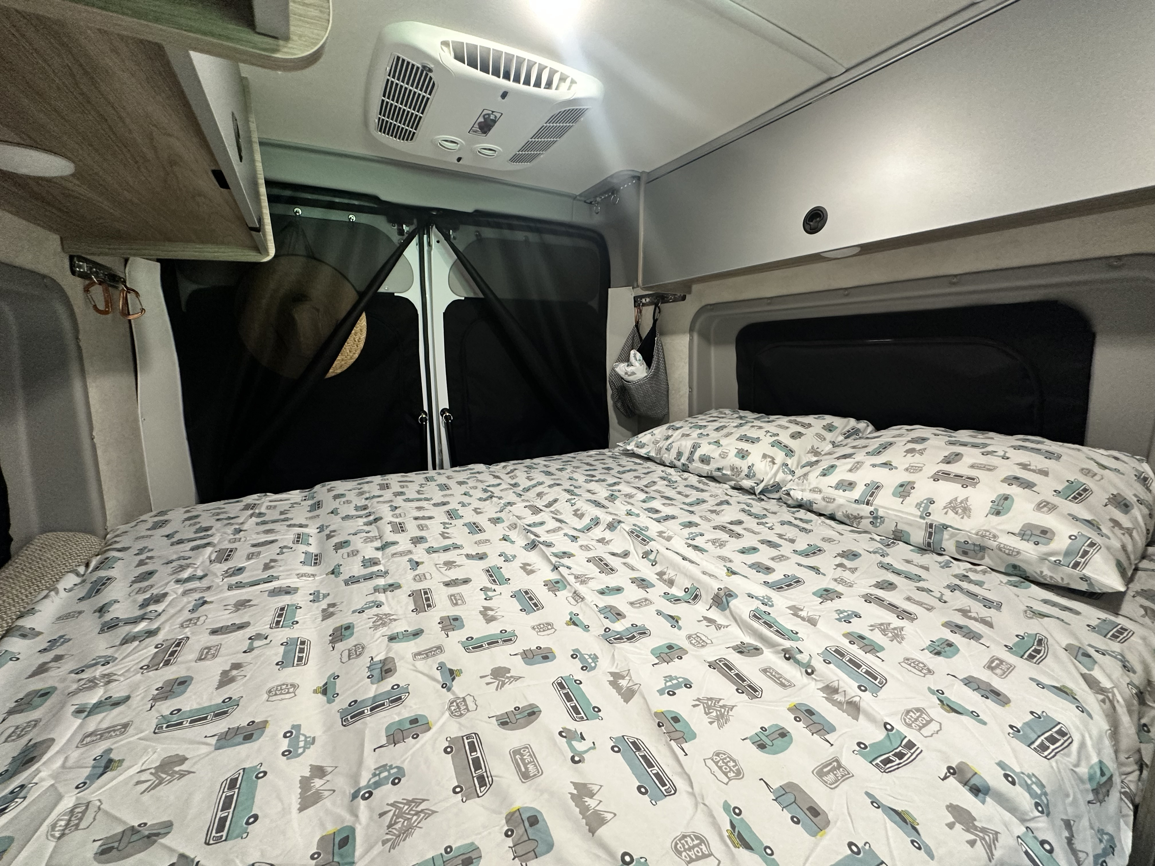 Inside this cozy RV rental, discover a comfortable bed with road trip themed sheets, overhead AC, and handy storage.. Winnebago Solis 2023