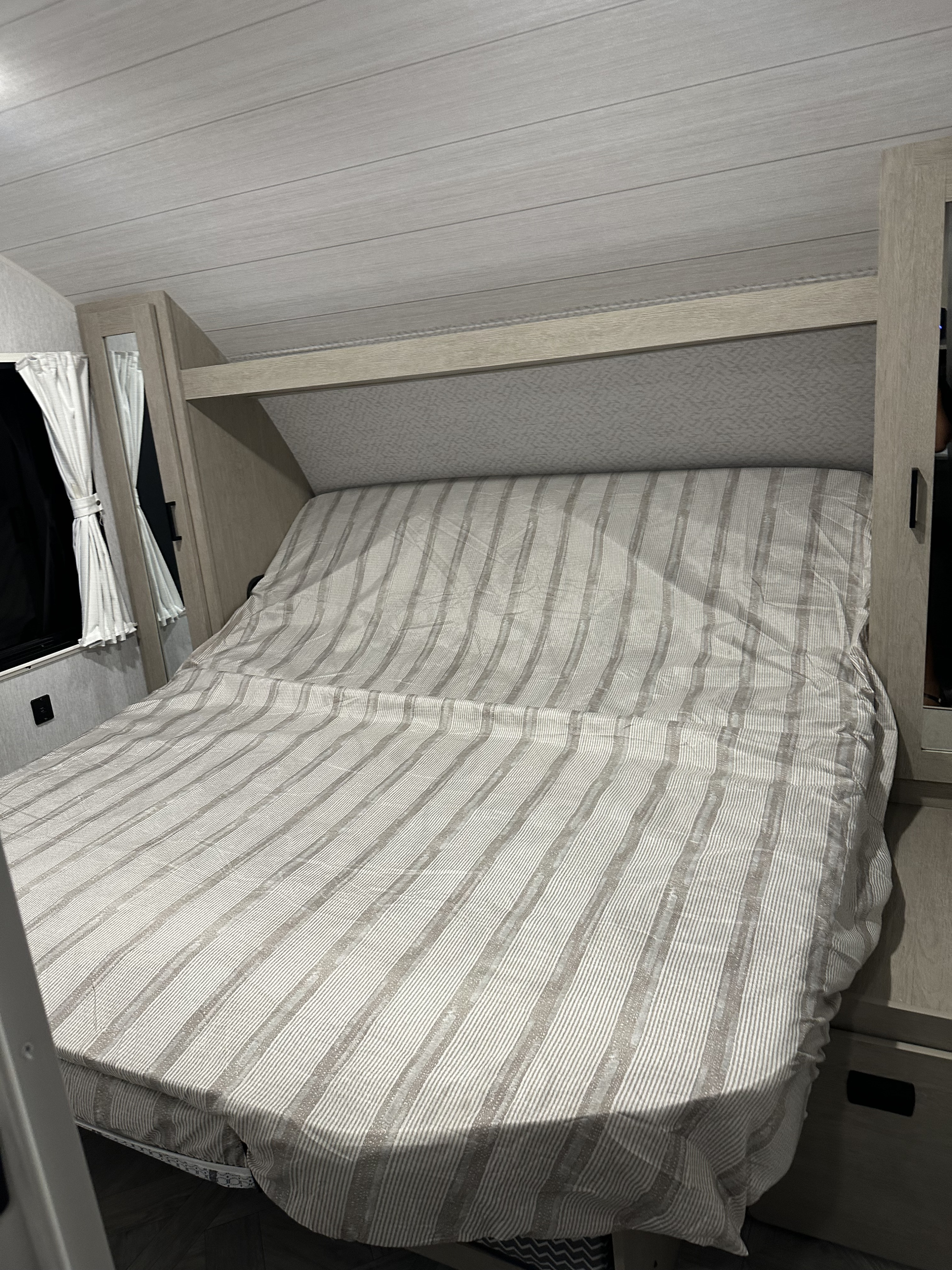 Cozy RV rental bedroom featuring a striped bed, built-in storage, and compact layout for comfortable travel.. Forest River Wild wood 2024