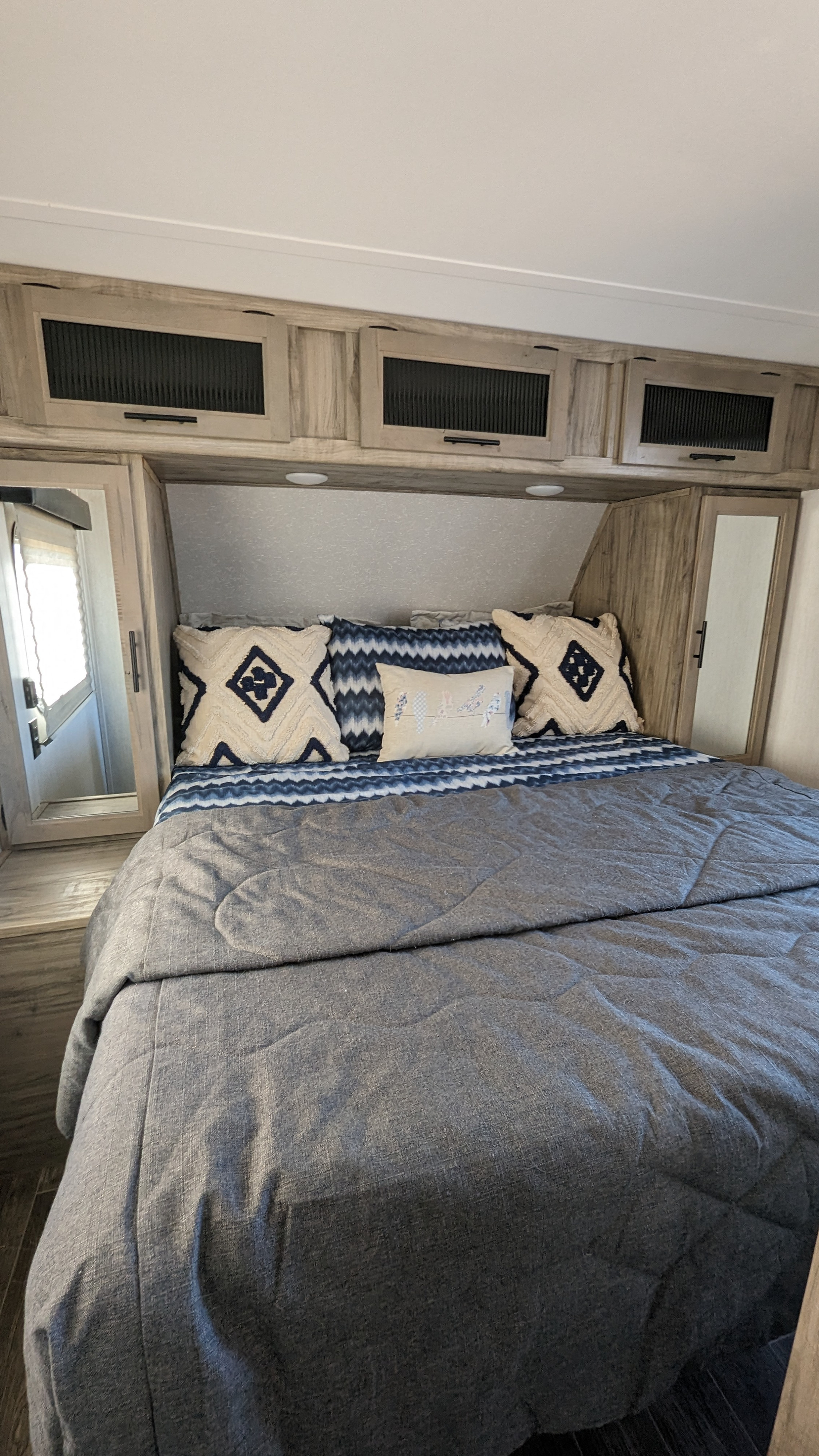 Cozy RV rental bedroom features a comfortable bed with decorative pillows, overhead storage, and mirrored cabinets, ideal for travel.. Forest River Cherokee Alpha Wolf 2021
