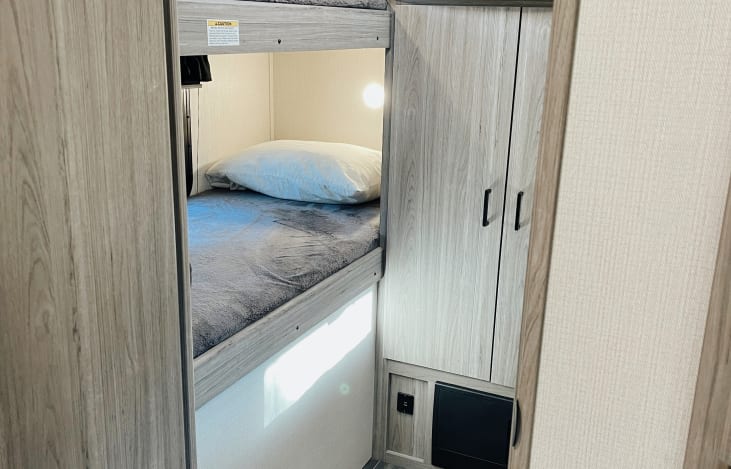 Inside an RV rental: a comfortable bunk bed setup with reading light & storage. Perfect for family adventures.. Keystone RV Passport SL 2022