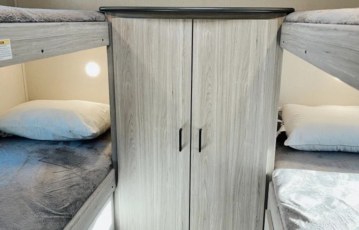 Inside an RV rental: two bunk beds with pillows & blankets, flanking a tall storage cabinet. Ideal for family camping trips.. Keystone RV Passport SL 2022