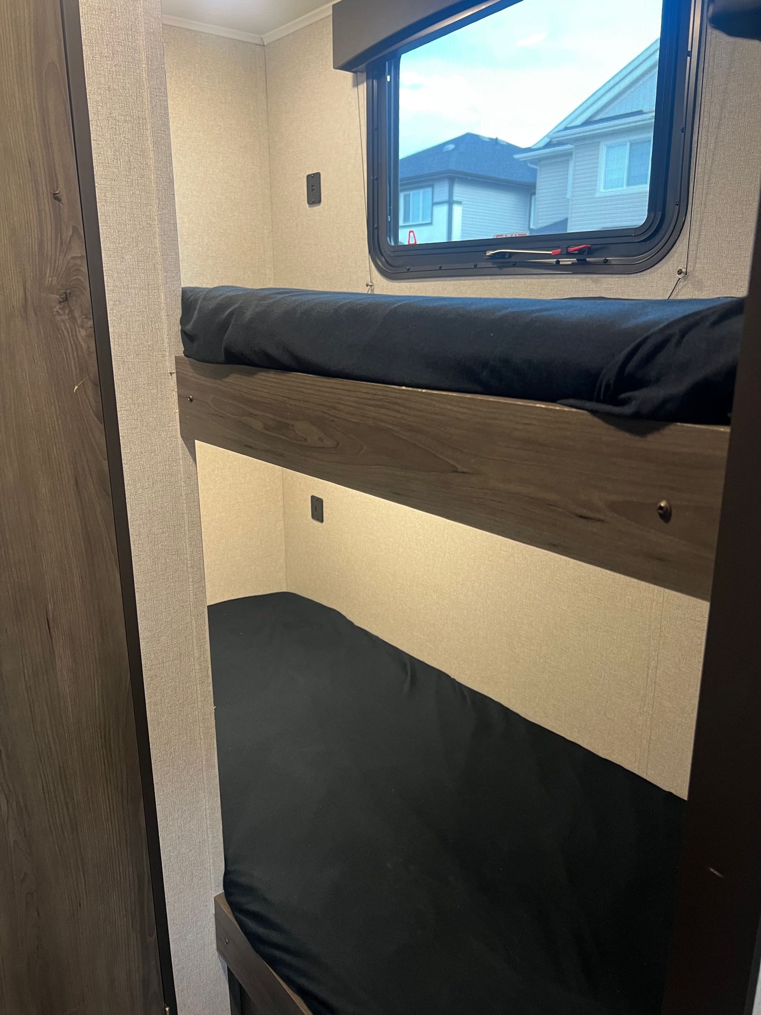 Inside an RV rental: black-sheeted bunk beds provide cozy travel accommodation. A window offers views outside.. Viking 1706 2021
