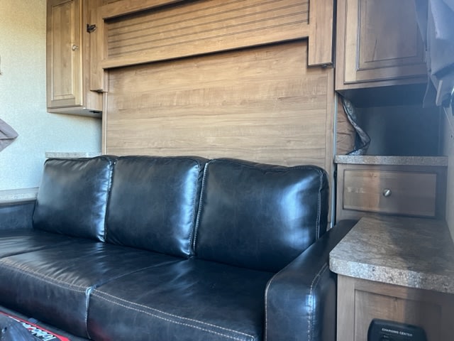 Spacious RV rental interior featuring a comfortable black sofa, a built-in wall bed, and wood cabinets with storage.. Forest River Rockwood Mini Lite 2018