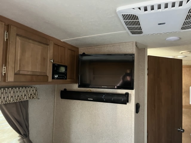 Inside an RV rental: entertainment setup with a TV, soundbar, stereo, and wooden cabinets. Overhead AC unit visible.. Forest River Rockwood Mini Lite 2018