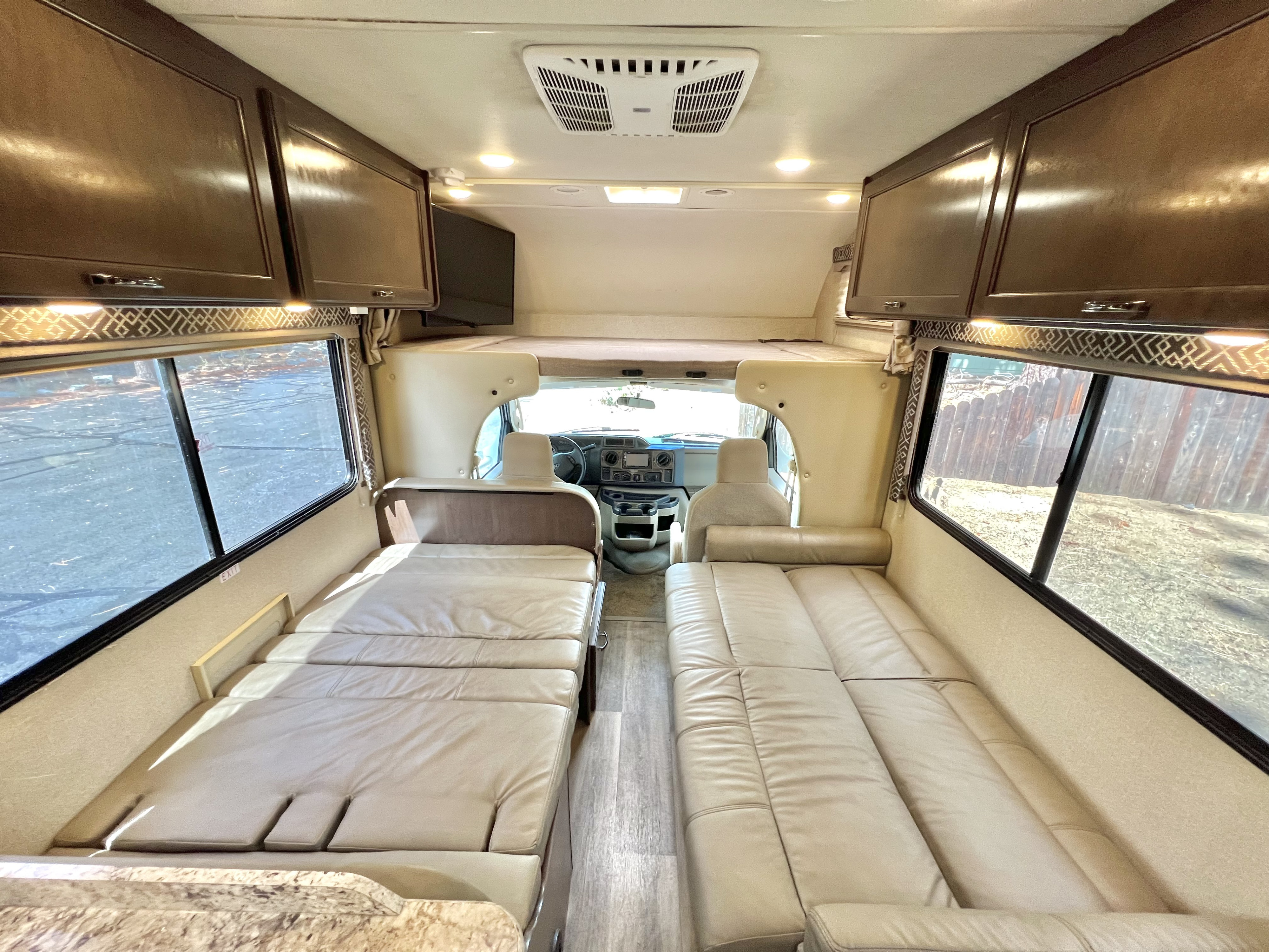 Spacious RV rental interior featuring two convertible beds, ample overhead cabinets, and a clear view of the front cab.. Thor Four Winds 2018