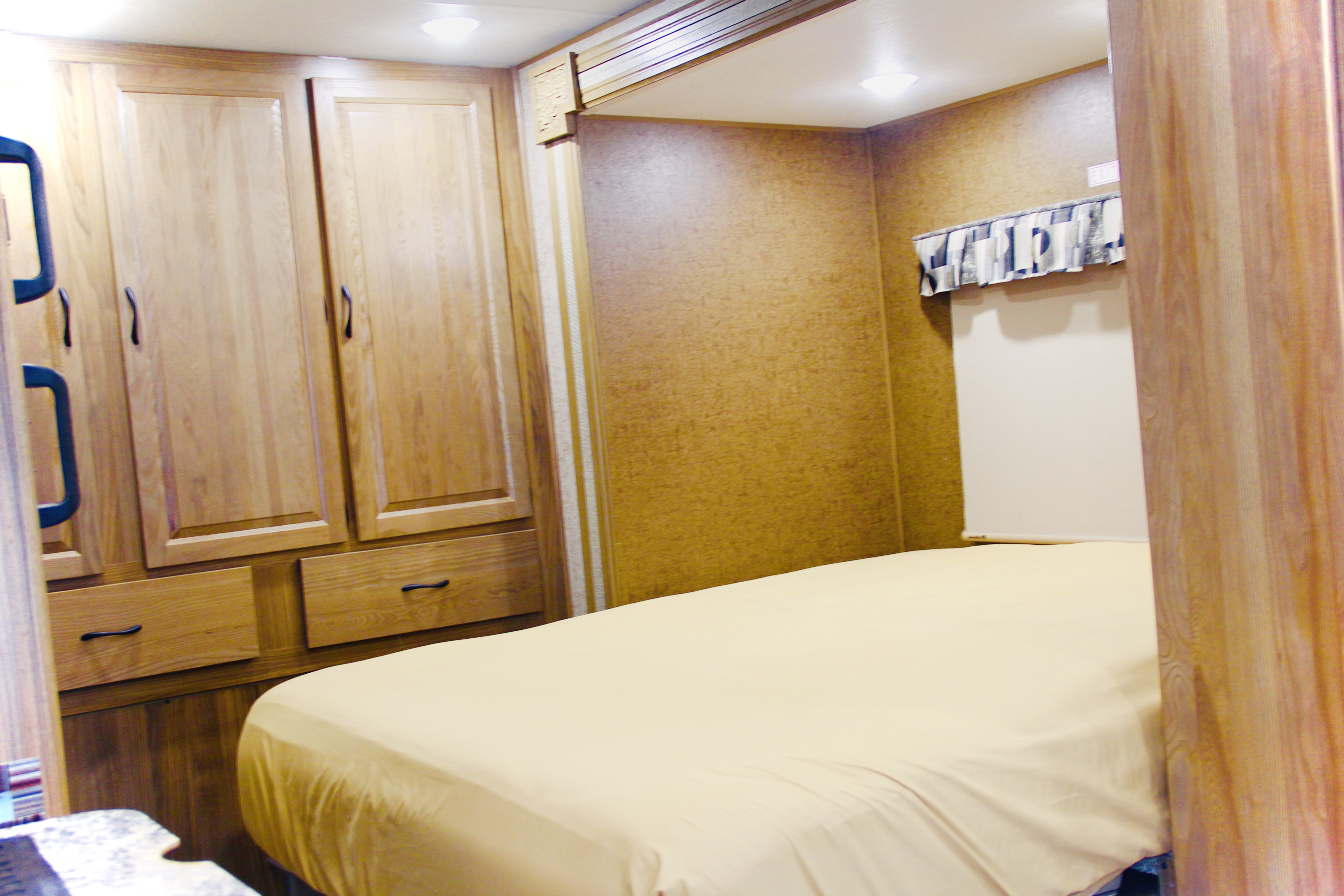 RV rental bedroom featuring a comfortable bed, overhead lighting, built-in wooden cabinets and drawers, and textured walls.. Forest River Coachmen Prism 2018