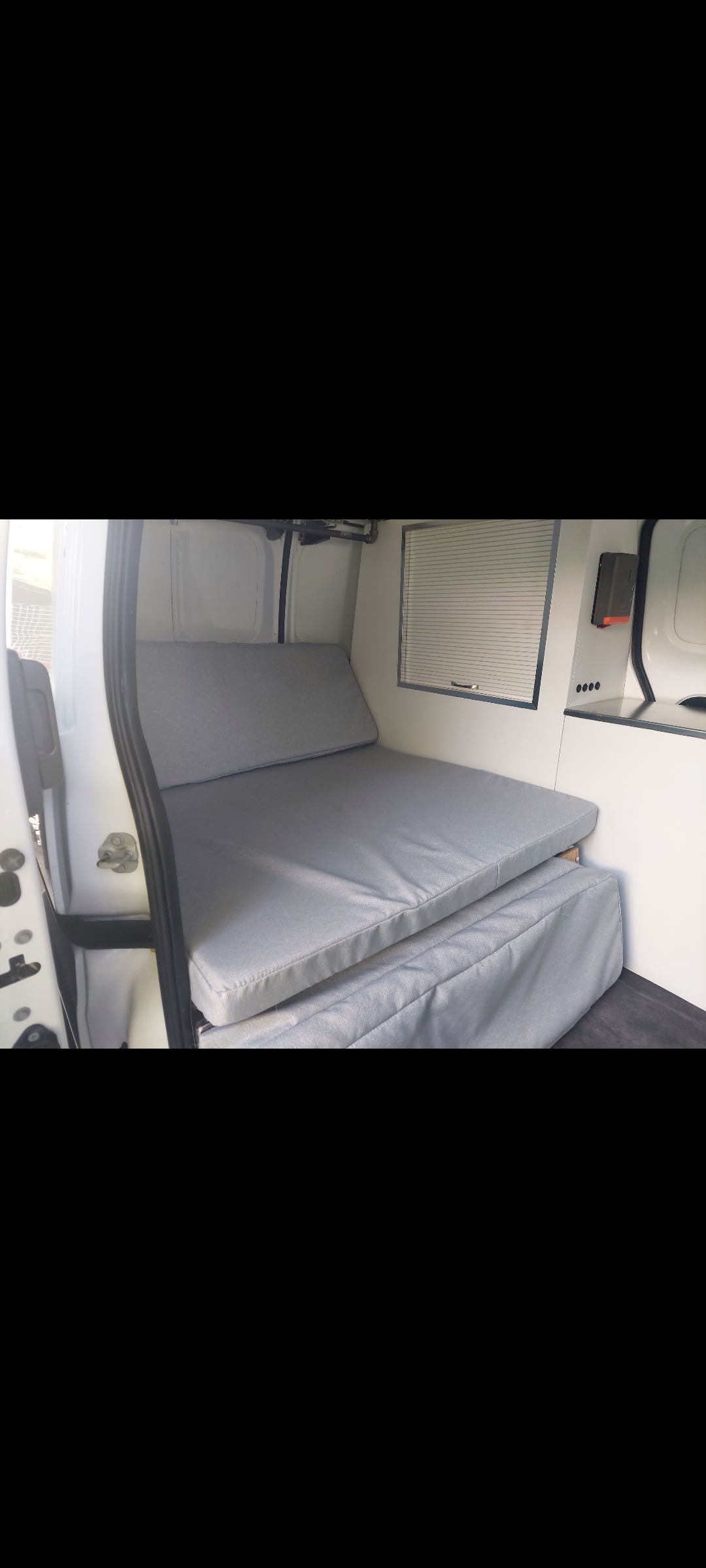 Modular grey bed/seating in a white RV rental interior, ideal for versatile camper van sleeping and relaxing.. NISSAN NV200 2013