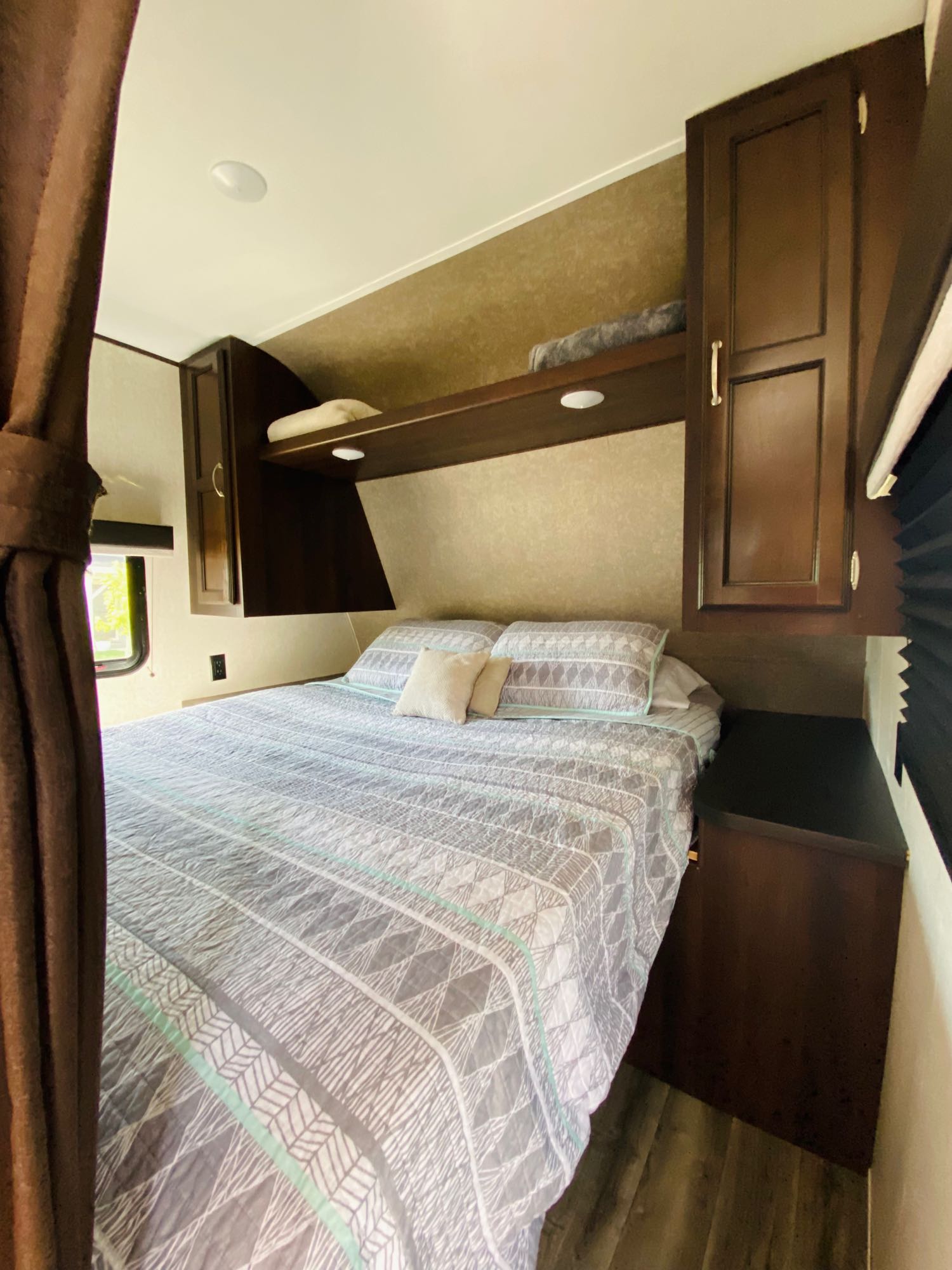 RV rental bedroom showcasing a queen bed with patterned bedding, dark wood cabinets, and shelves for storage.. Jayco Jay Flight SLX 2018
