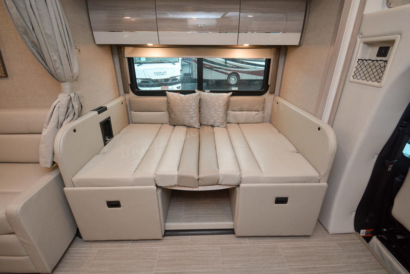 RV rental interior: versatile cream convertible bed and living area with overhead storage. Perfect for RV travel.. Thor Motor Coach Delano 2023