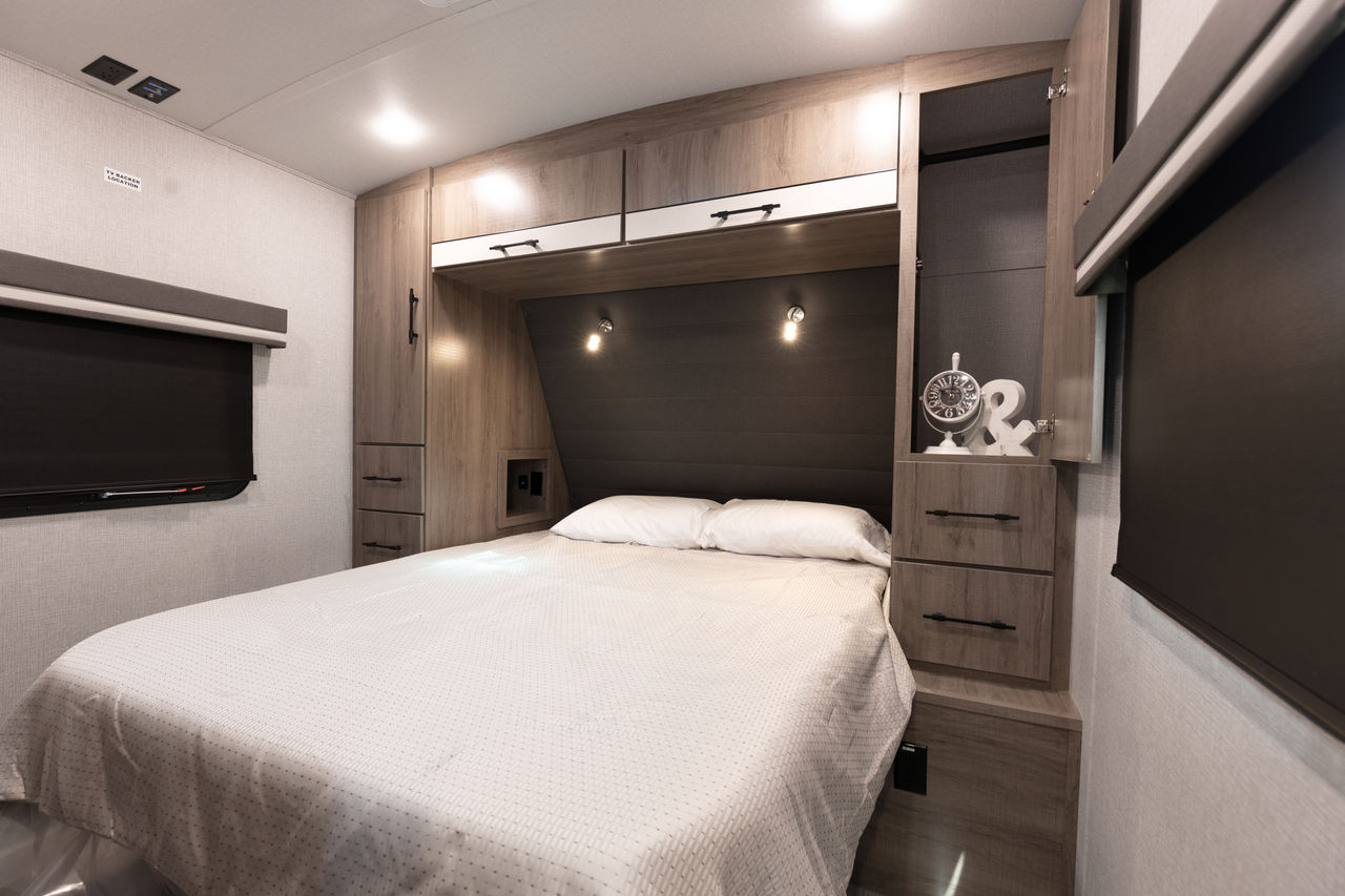 Full-size bed, overhead cabinets, and sconce lighting define this cozy RV rental bedroom. Perfect for your next adventure.. Grand Design Imagine 2021