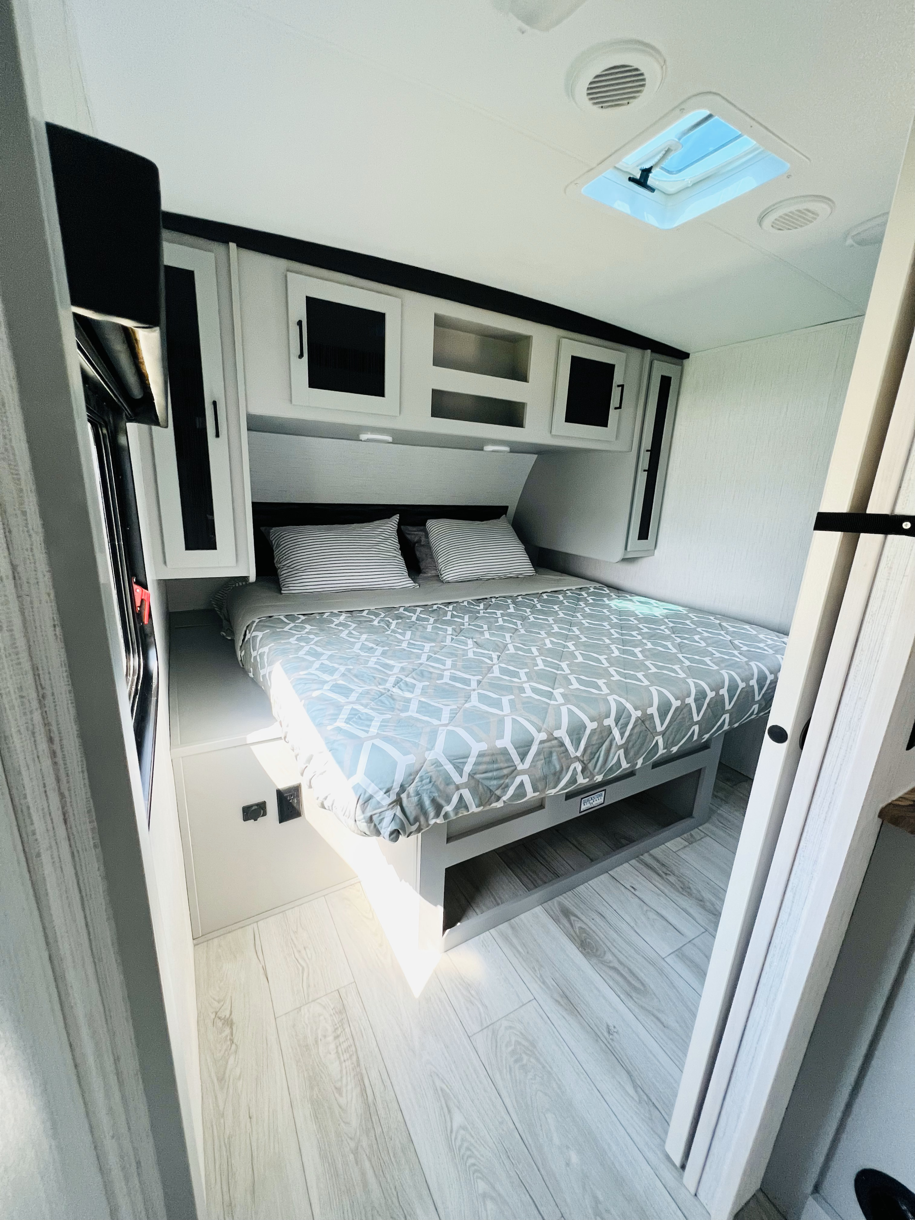 Interior of an RV rental bedroom showing a bed with a patterned comforter, overhead cabinets, and a ceiling skylight.. Heartland RVs North Trail 2022
