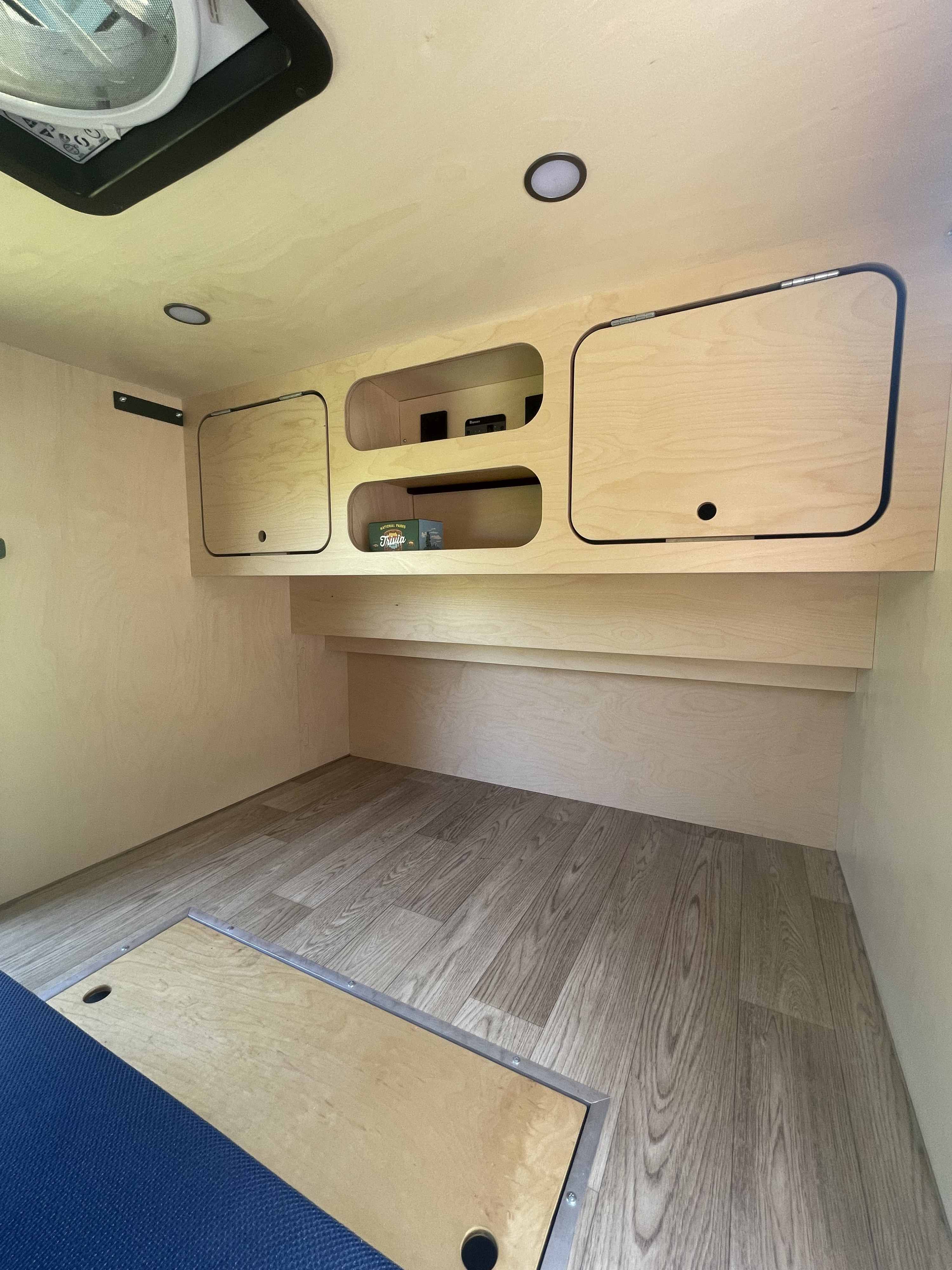 Clean and bright RV rental interior showcasing light wood paneling, built-in storage, and modern wood-look flooring.. TG Customs Teardrop 2023