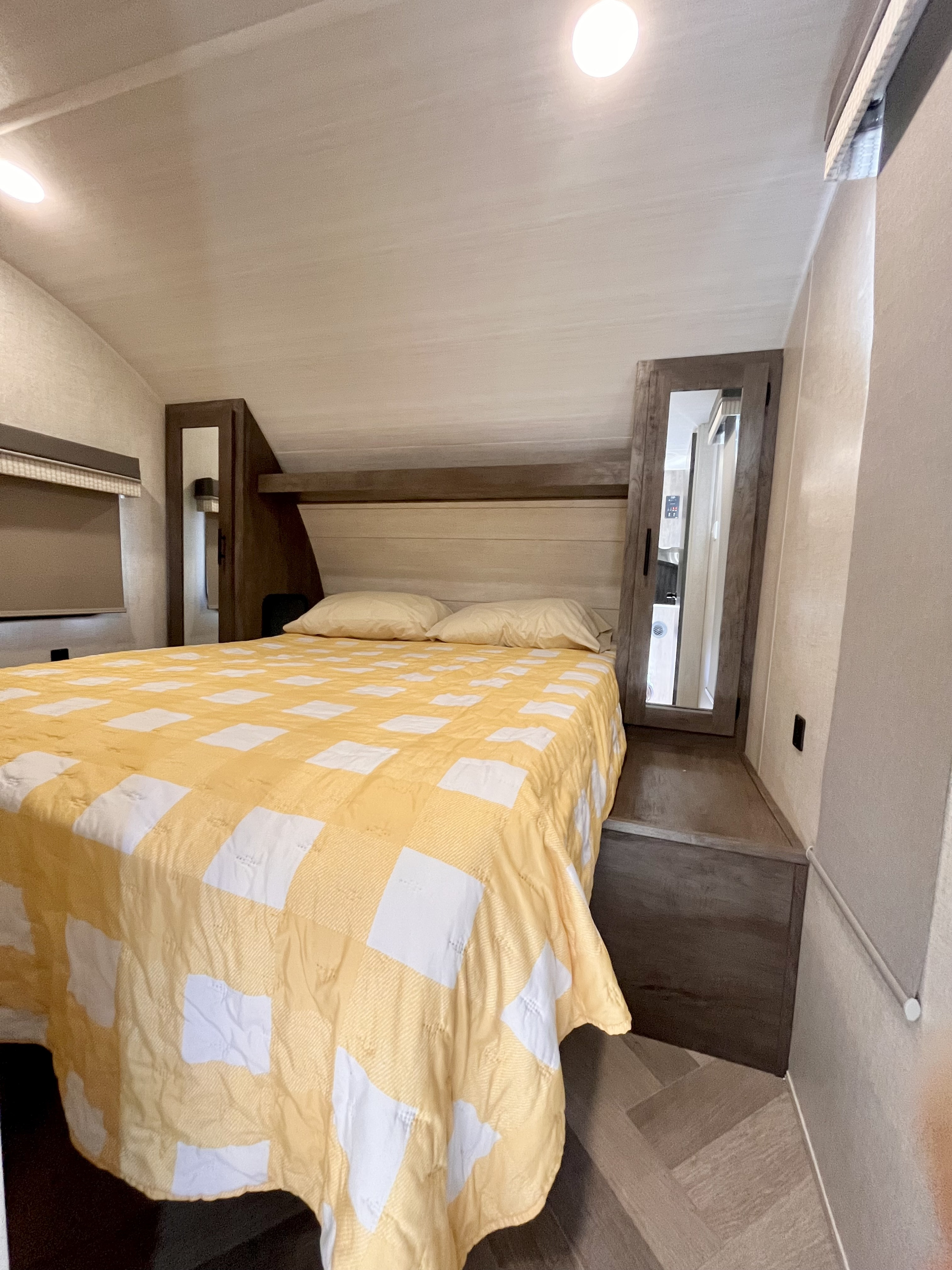 This RV rental bedroom features a bed with a yellow checkered quilt, two pillows, built-in storage, and a mirror.. Forest River Salem Cruise Lite 2021