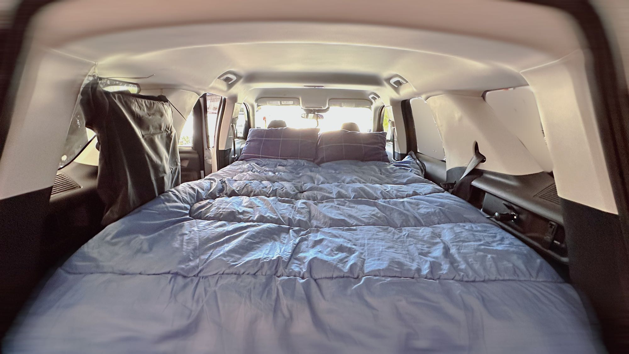 Interior of a vehicle set up as a comfortable bed with blue bedding and pillows, ideal for an RV rental-style car camping trip.. Ford Bronco Sport 2022