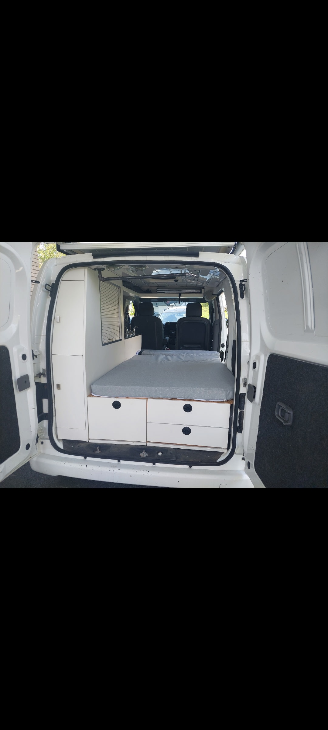 RV rental interior: A white van converted with a comfortable bed, drawers for storage, and a small kitchenette area.. NISSAN NV200 2013