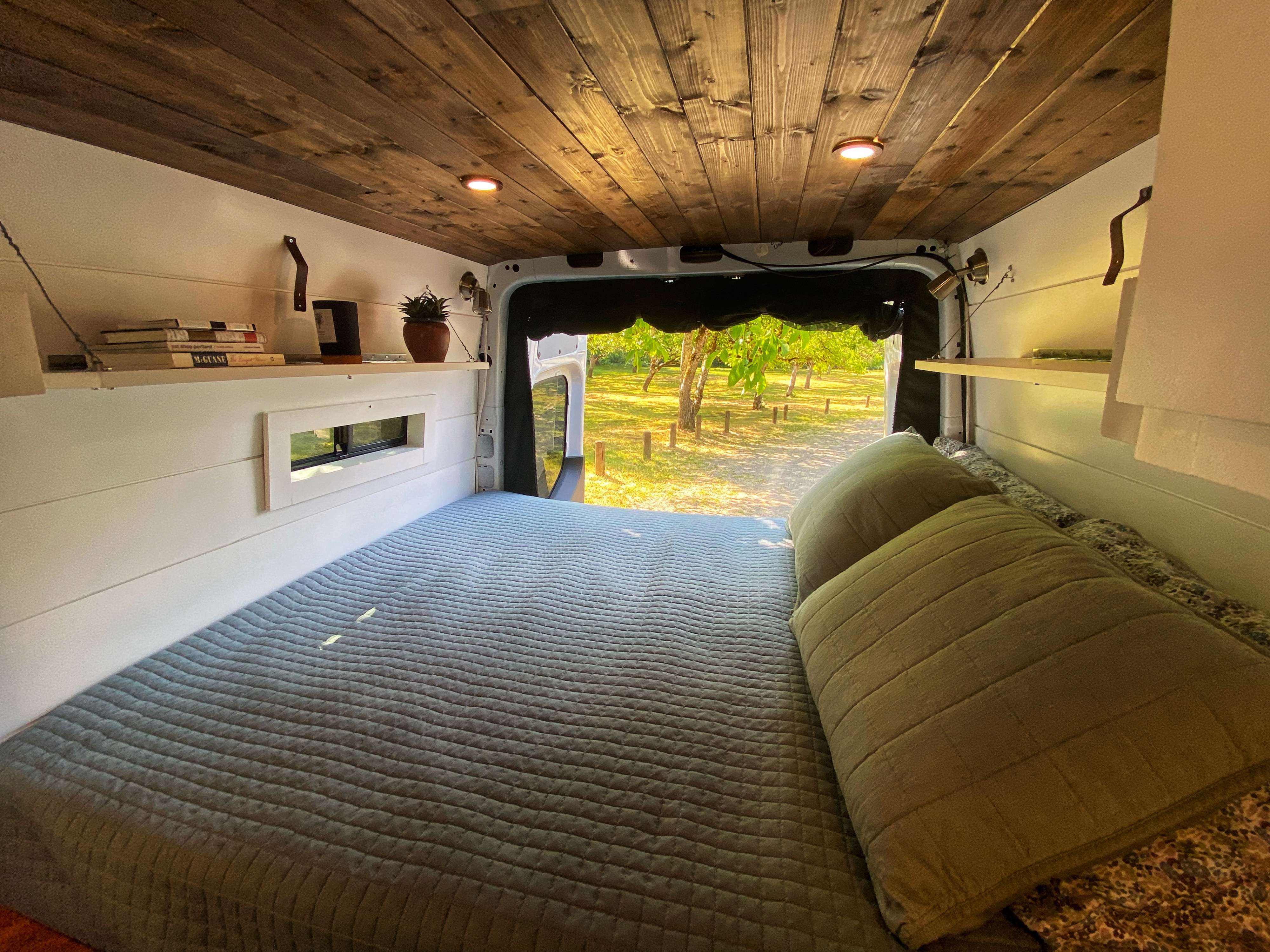 Cozy RV rental: interior bedroom with a comfy bed, wooden ceiling, and scenic park view from the open back.. Freightliner Sprinter 2020