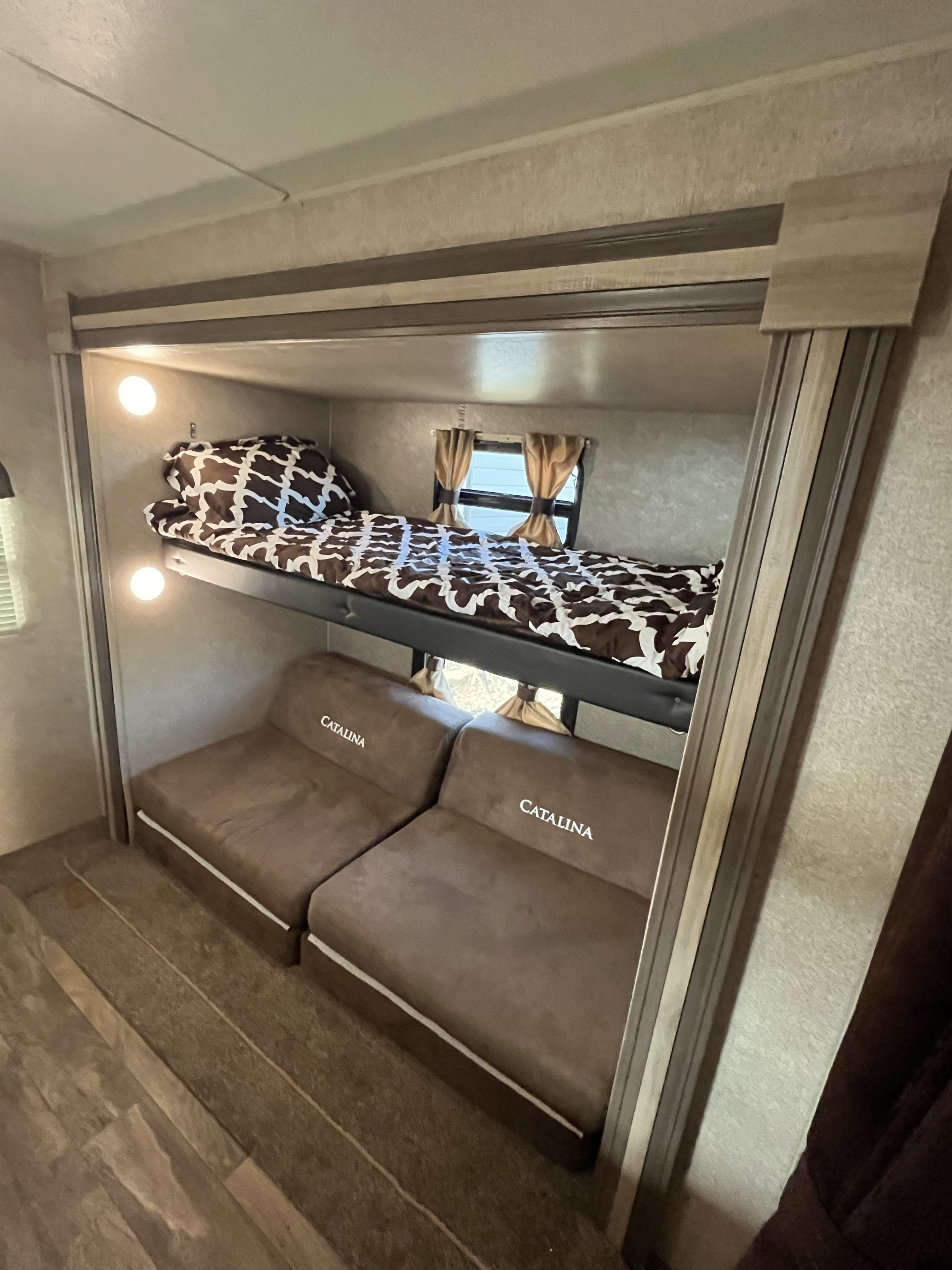 An RV rental's compact bunk area, featuring an upper bed with brown and white bedding, and two lower "Catalina" brown seat cushions.. Coachmen Catalina 2019
