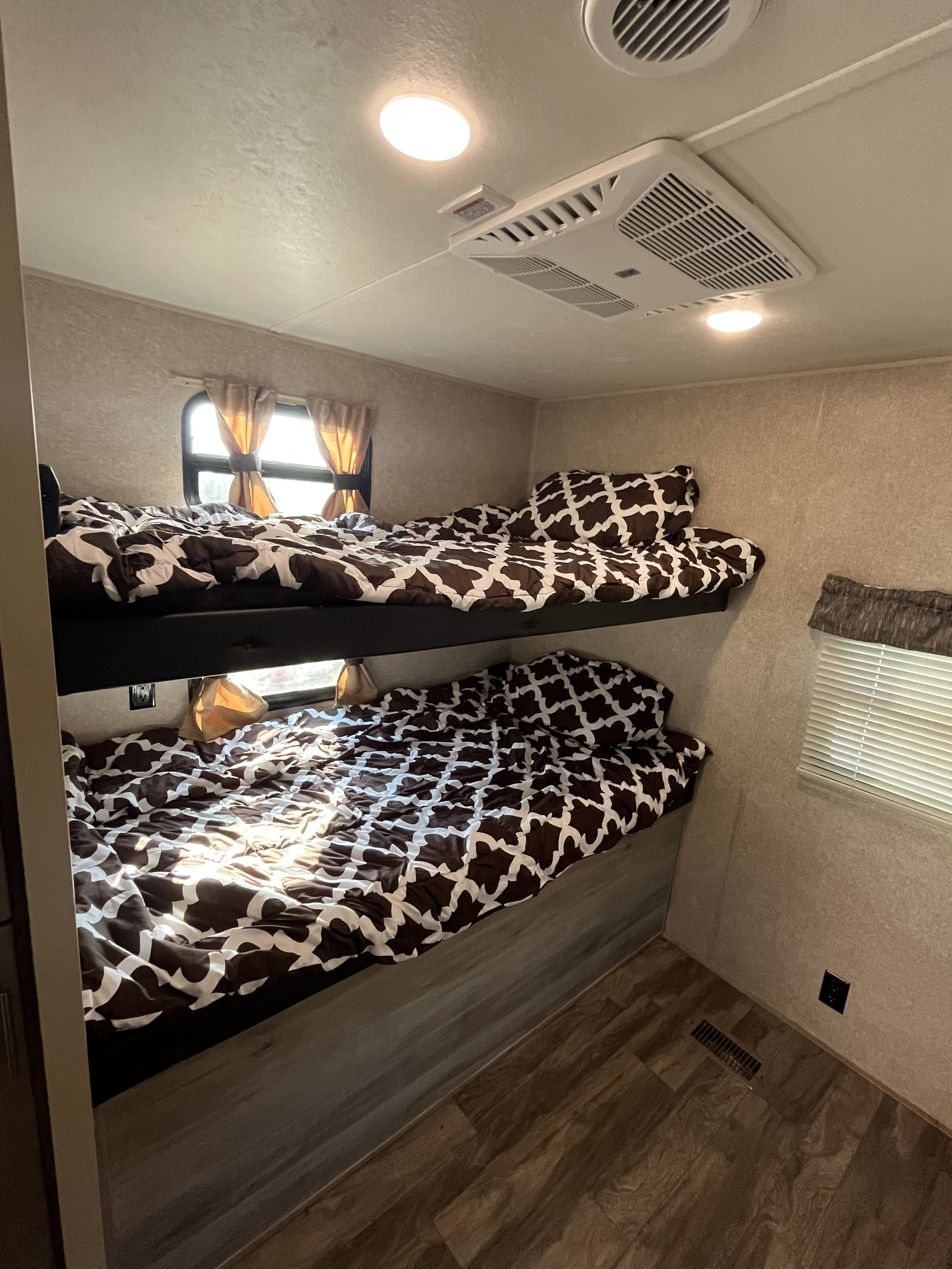 Inside an RV rental: two neatly made bunk beds with brown & white patterned bedding, featuring windows and AC for comfort.. Coachmen Catalina 2019