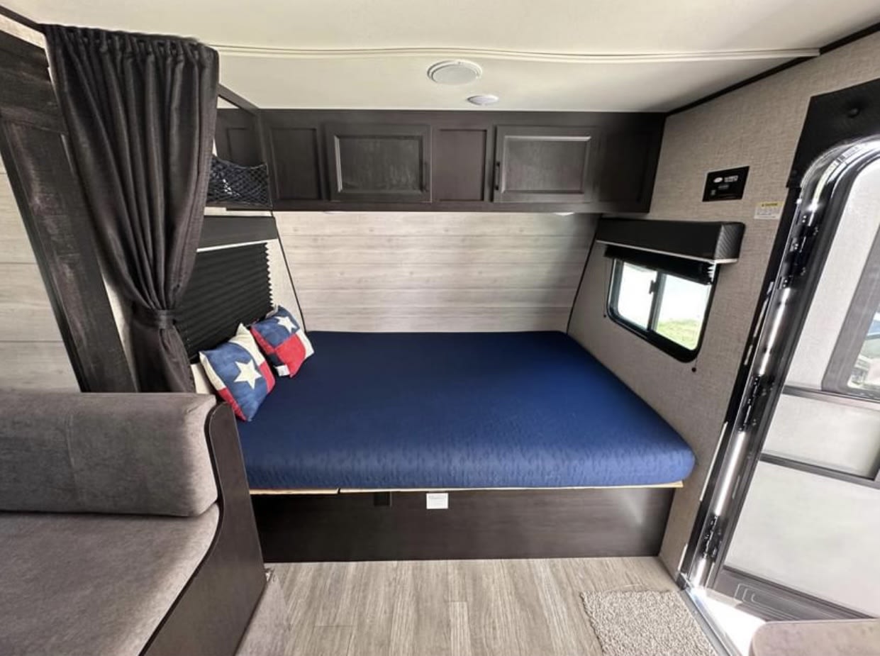 Inside this RV rental: a compact bedroom with a queen bed, blue mattress, Texas flag pillows, overhead cabinets, and a side sofa.. Jayco Jay Flight SLX 2022