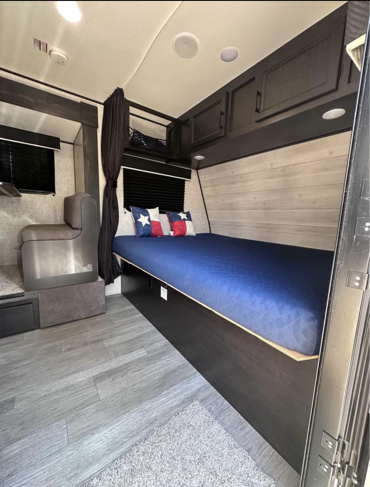 RV rental interior: A compact, modern living space with a blue bed, Texas flag pillows, and a grey dinette. Overhead storage visible.. Jayco Jay Flight SLX 2022