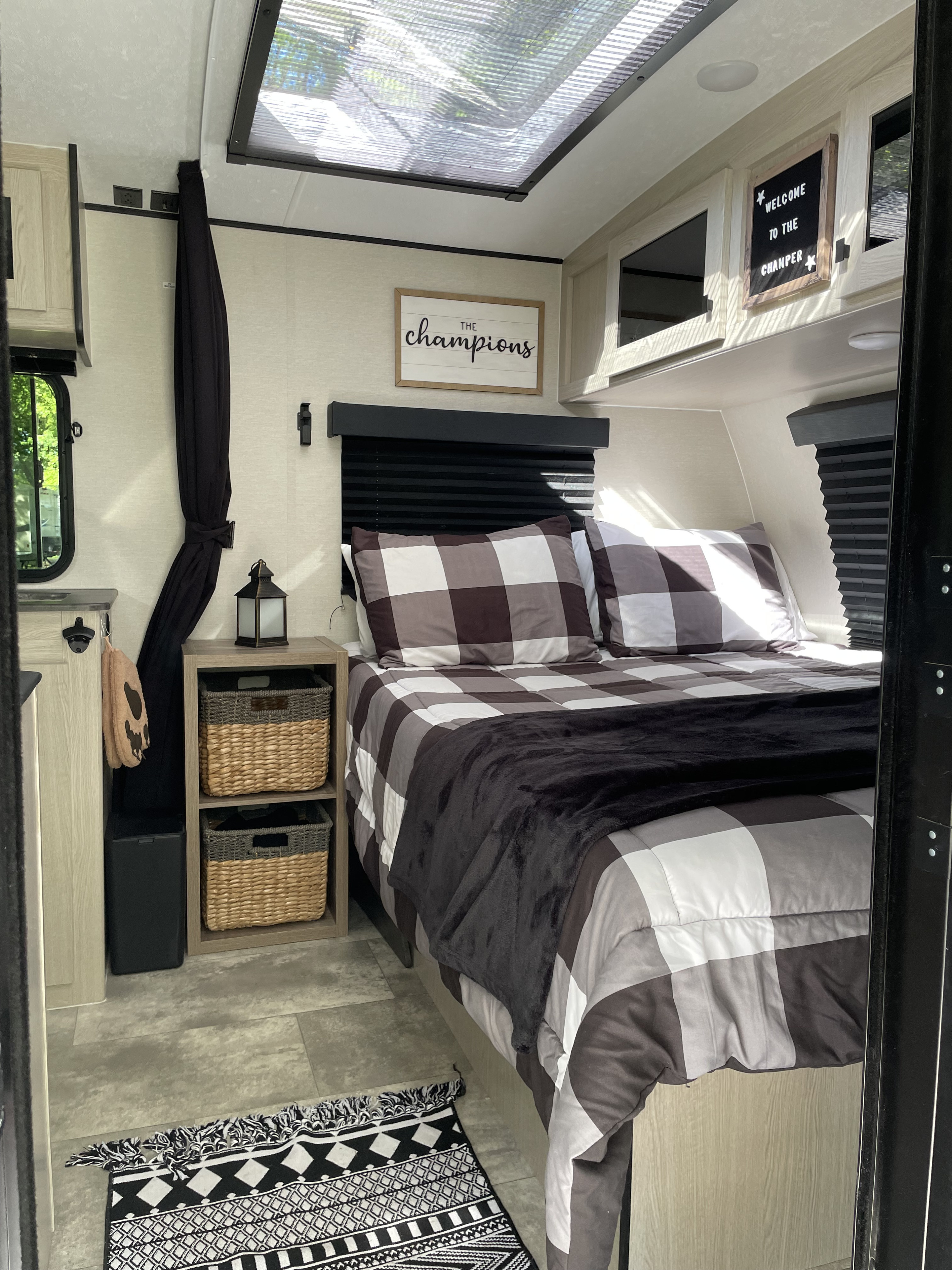 Cozy rv rental bedroom features a comfy plaid bed, woven baskets, and charming wall decor under a skylight.. Coachmen Apex Nano 2023