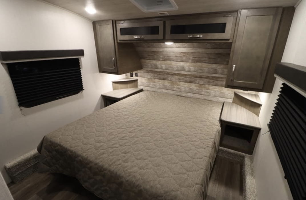 Well-appointed RV rental bedroom with a comfortable bed, wood-paneled headboard, overhead cabinets, and built-in nightstands.. Keystone RV Cougar 2023