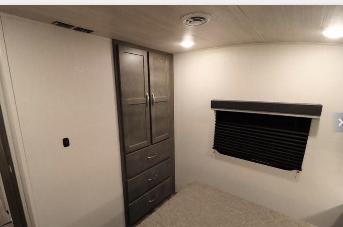 RV rental bedroom featuring a built-in wardrobe with drawers, a window with black blinds, and part of the bed.. Keystone RV Cougar 2023