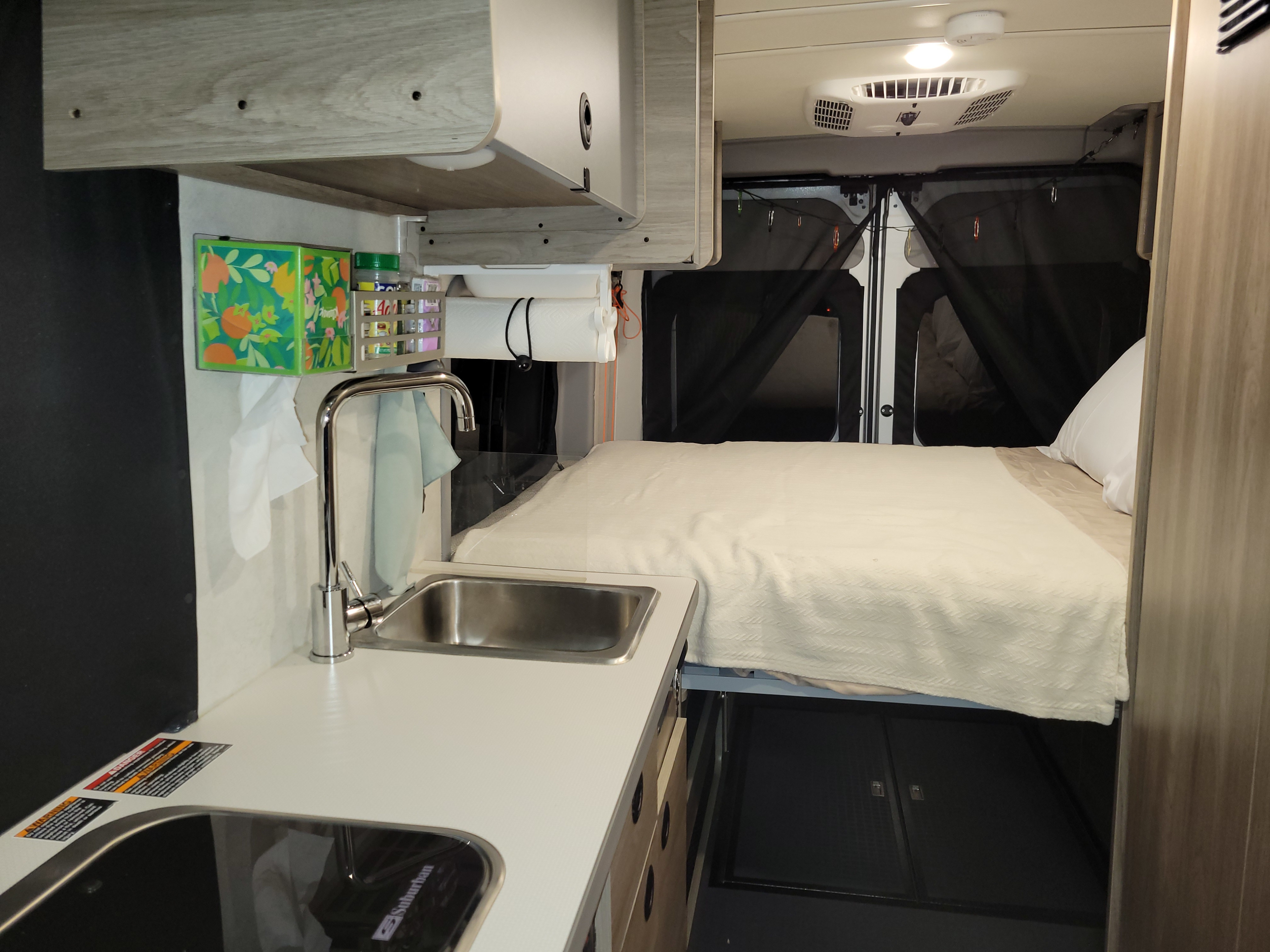 Inside an RV rental, discover the compact kitchen with sink, stovetop, and a cozy bed area.. Winnebago Solis 2023