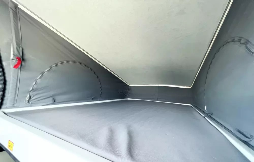 This photo shows a spacious RV rental pop-top, featuring a gray sleeping area and fabric walls with zippered ventilation. Great for camper van trips.. Winnebago Solis 2023