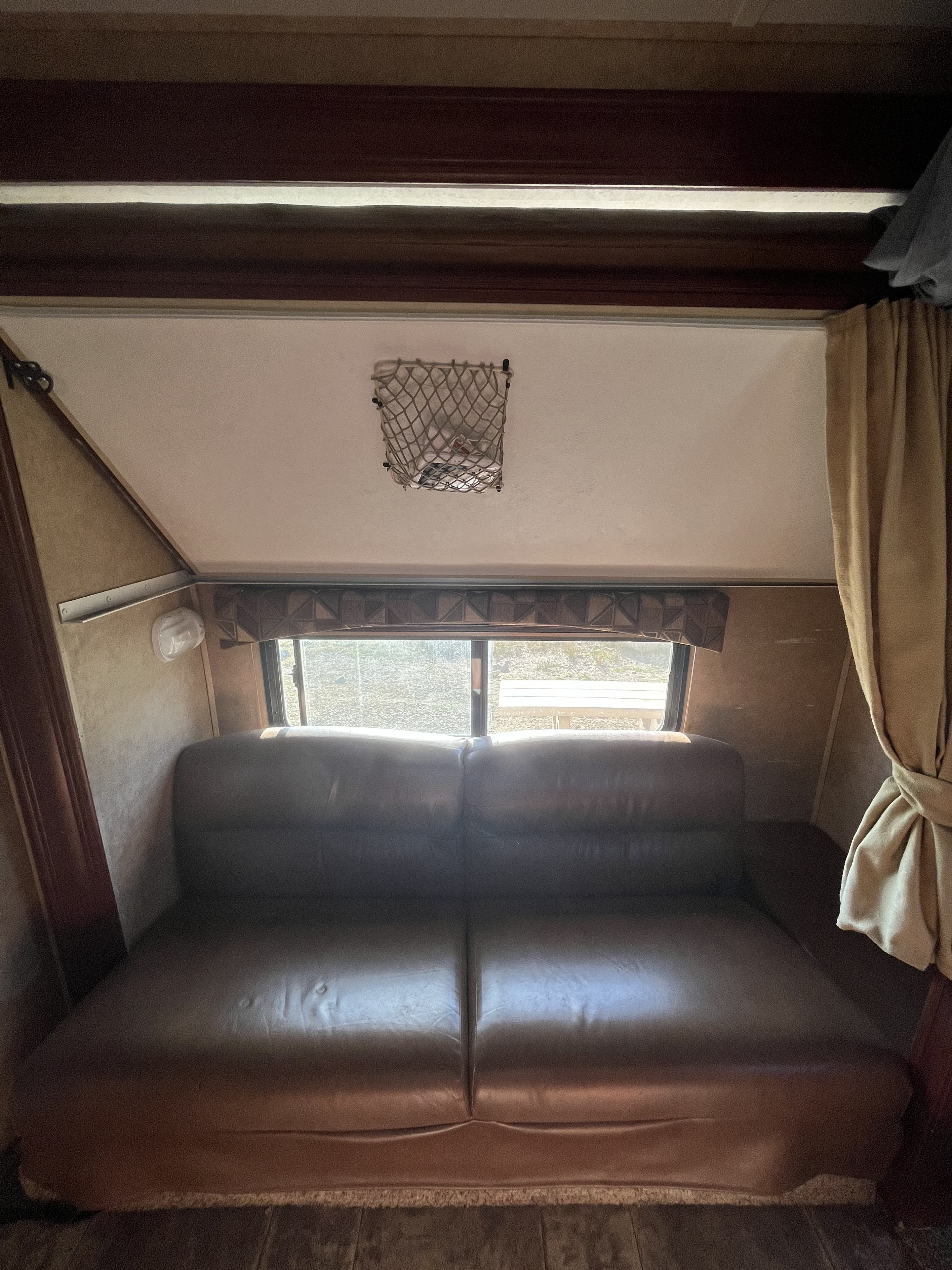Cozy RV rental interior showcasing a comfortable two-seater sofa, bright window, and practical ceiling storage net.. Forest River Sunseeker 2014