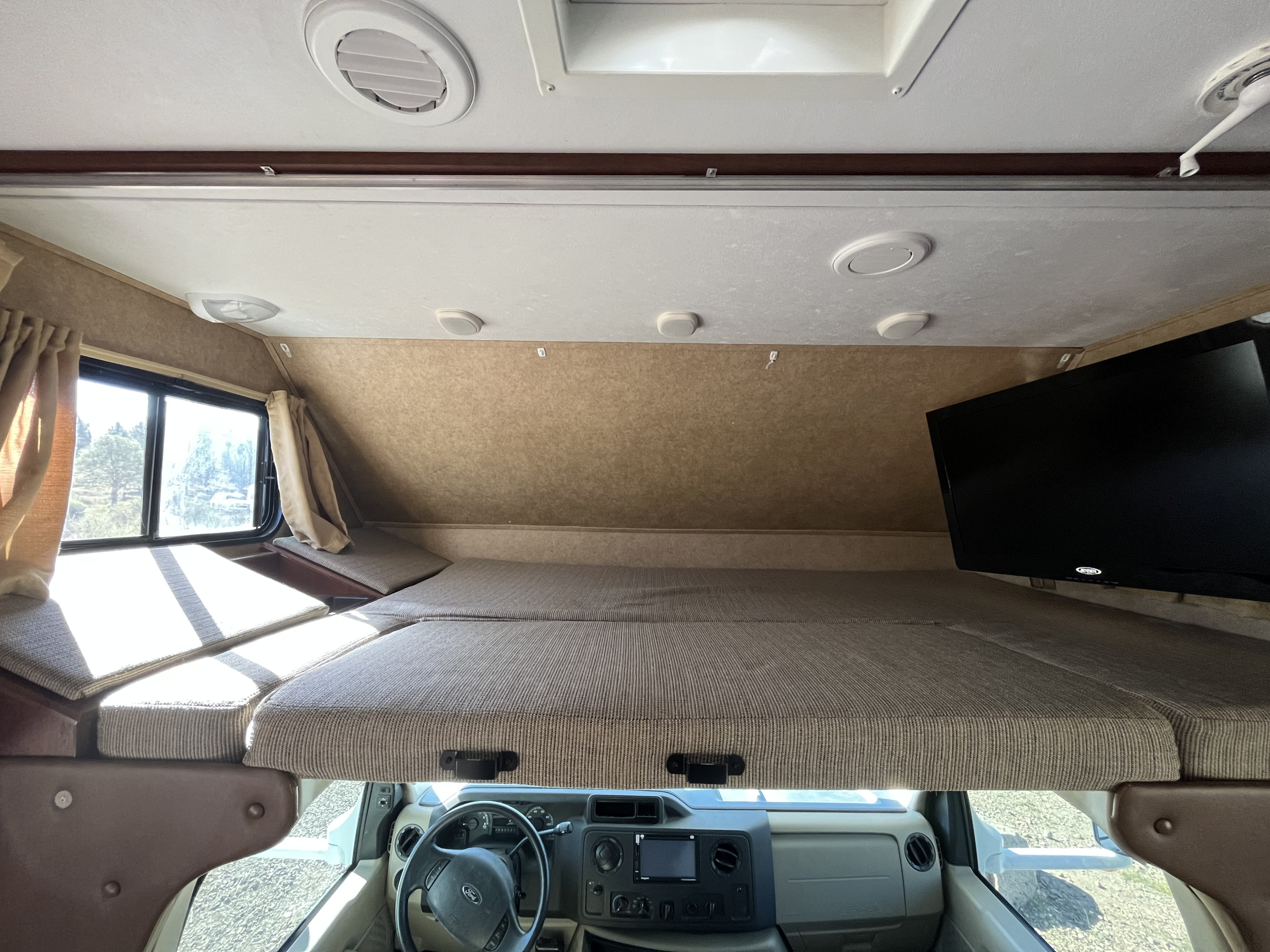 RV rental interior: cab-over bunk bed with mounted TV, window view, and front driver's area below.. Forest River Sunseeker 2014