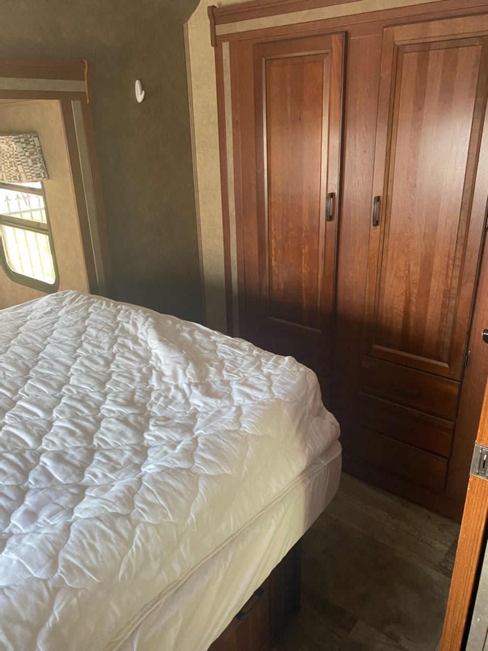 Inside an RV rental, a compact bedroom features a white mattress on a bed, wooden wardrobe, and window.. Forest River Sunseeker 2016