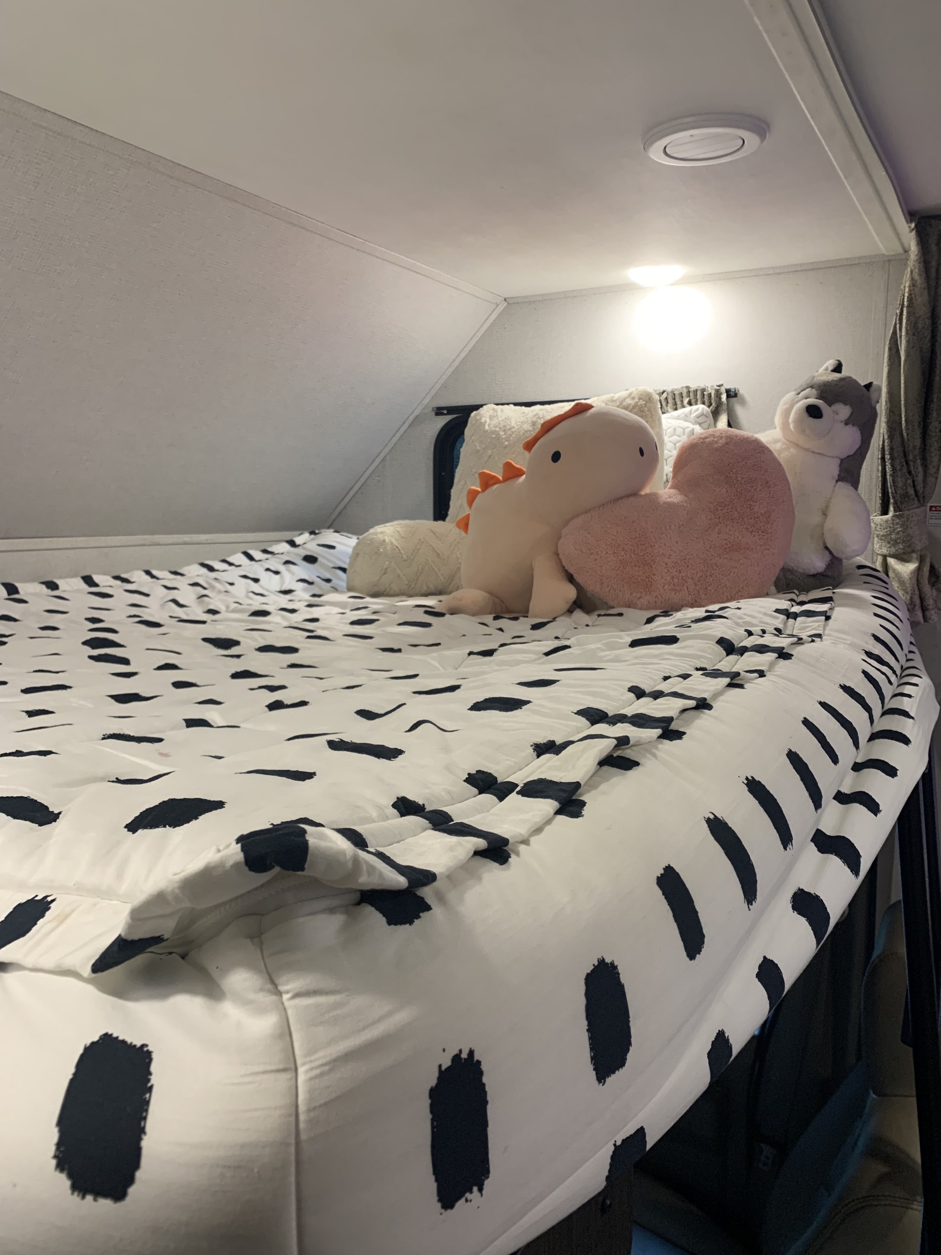 Cozy RV rental bed with black and white dash pattern bedding, plush dinosaur, heart, and husky on a built-in bunk.. Forester Classic 2021