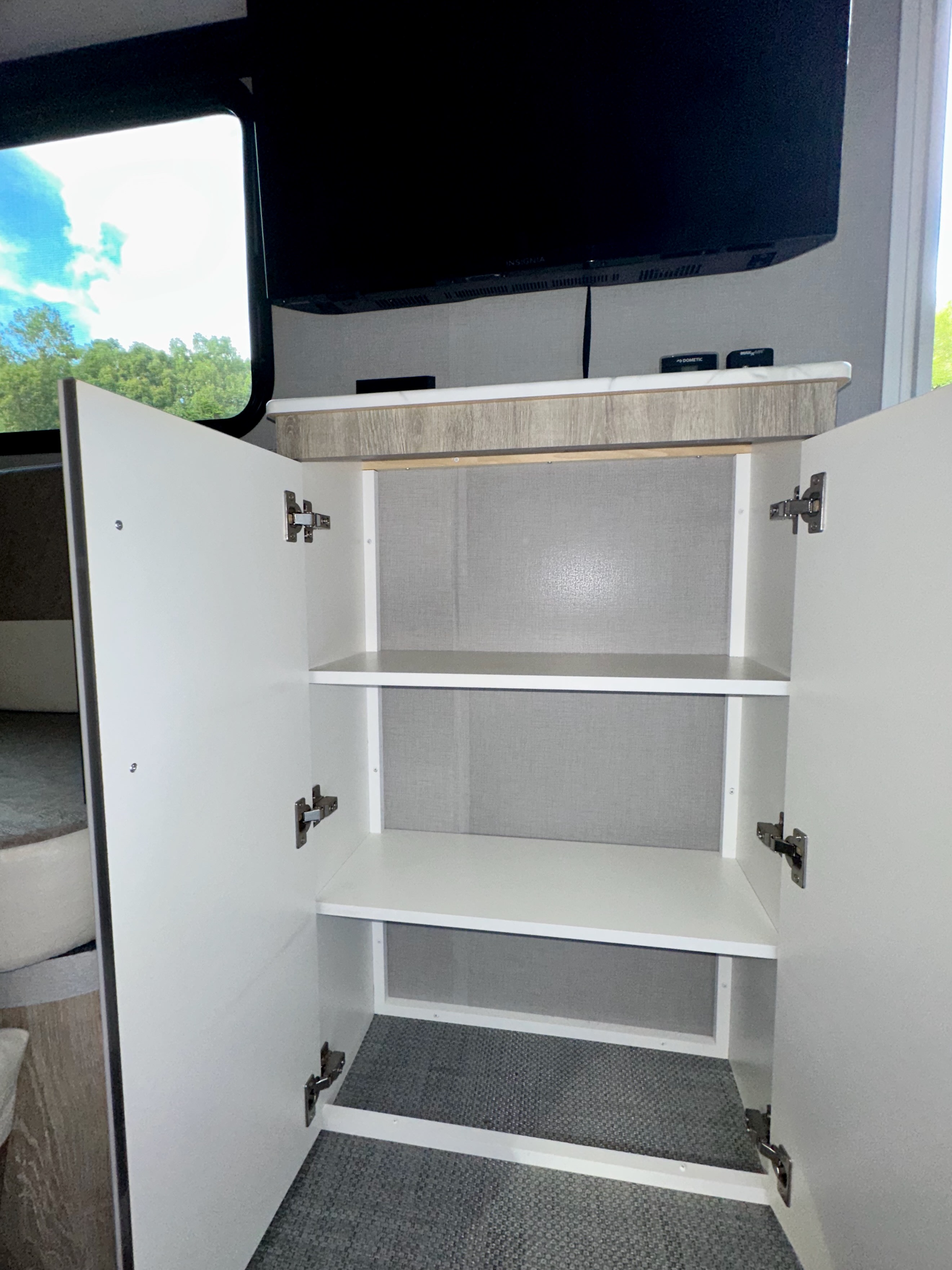 Spacious RV rental interior featuring an open storage cabinet with multiple shelves, a TV, and countertop.. InTech RV Sol 2022
