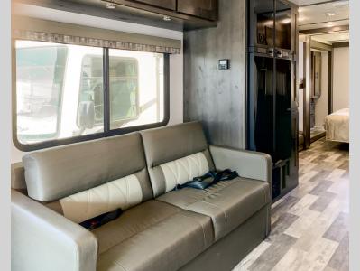 RV rental living space with a comfy sofa (with seatbelts), large window, and peek into the bedroom. Ideal for road trips and camping!. FR3 32DS 2024