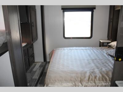 RV rental bedroom with comfortable bed, bright window, nightstand, and built-in storage.. FR3 32DS 2024