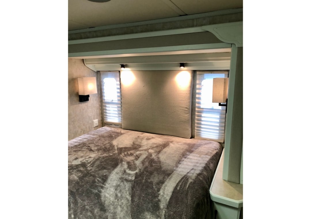 Cozy RV rental bedroom featuring a bed with a patterned blanket, window blinds, and ambient lighting for a comfortable stay.. Holiday Rambler Admiral SE 2004