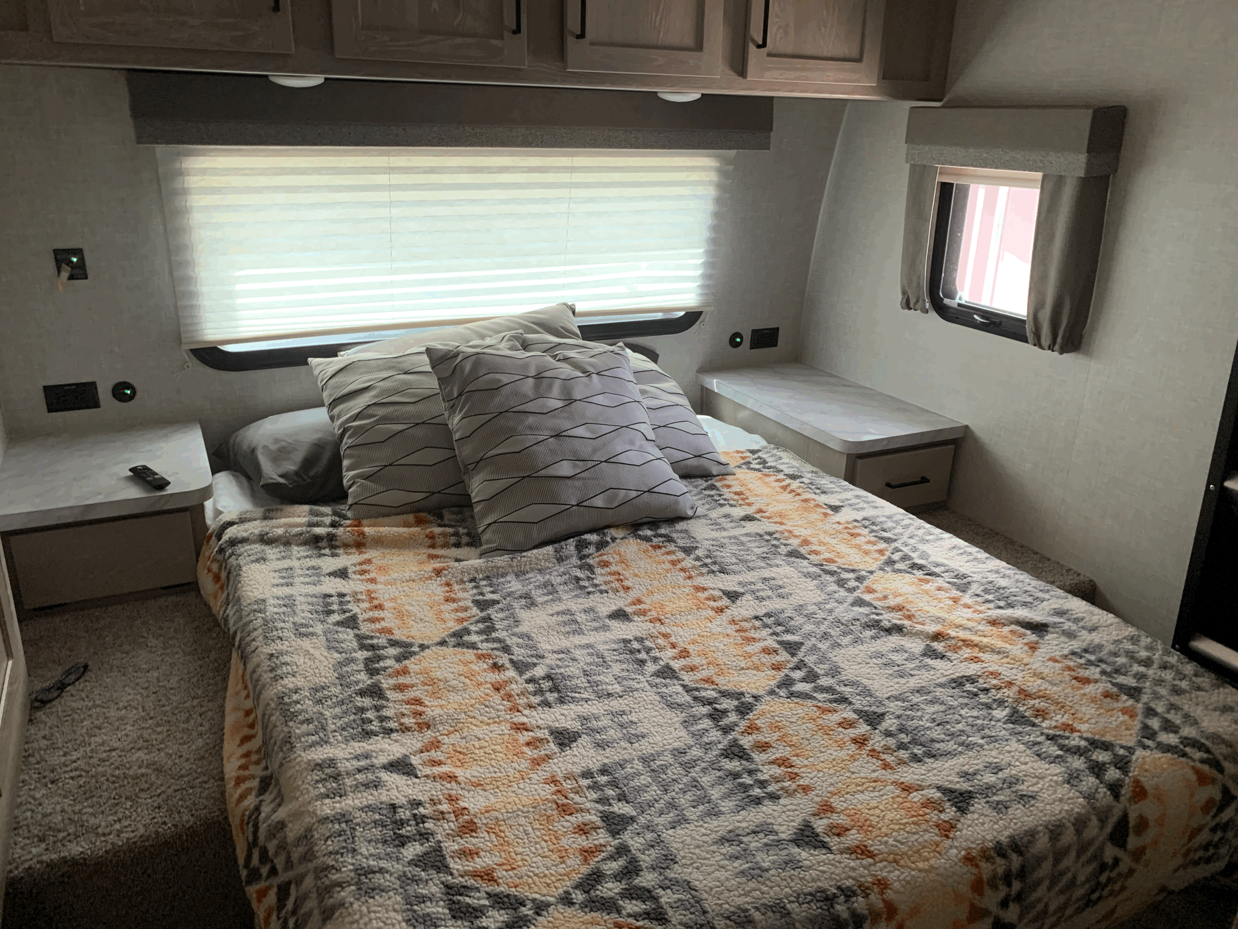 RV rental bedroom with a patterned blanket on the bed, overhead cabinets, bedside tables, and a large window.. Forest River Flagstaff Super Lite 2023