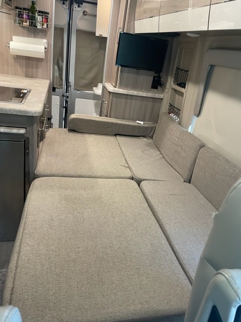 Spacious RV rental interior with a convertible bed, kitchen area, and mounted TV, showcasing comfortable living space.. Thor Motor Coach Scope 18M 2023