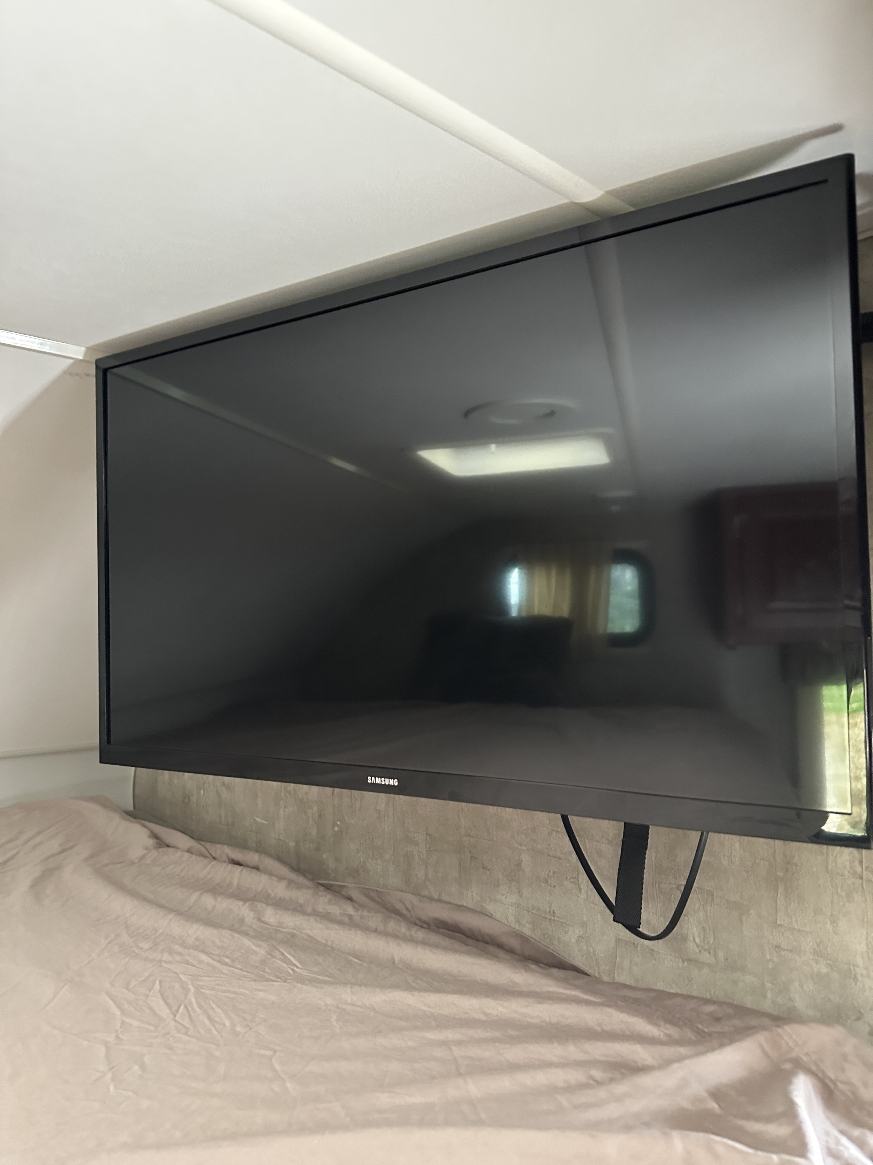 RV rental interior: Mounted Samsung TV above bed, reflecting ceiling light, window, and cabinet.. Winnebago Minnie Winnie 2014